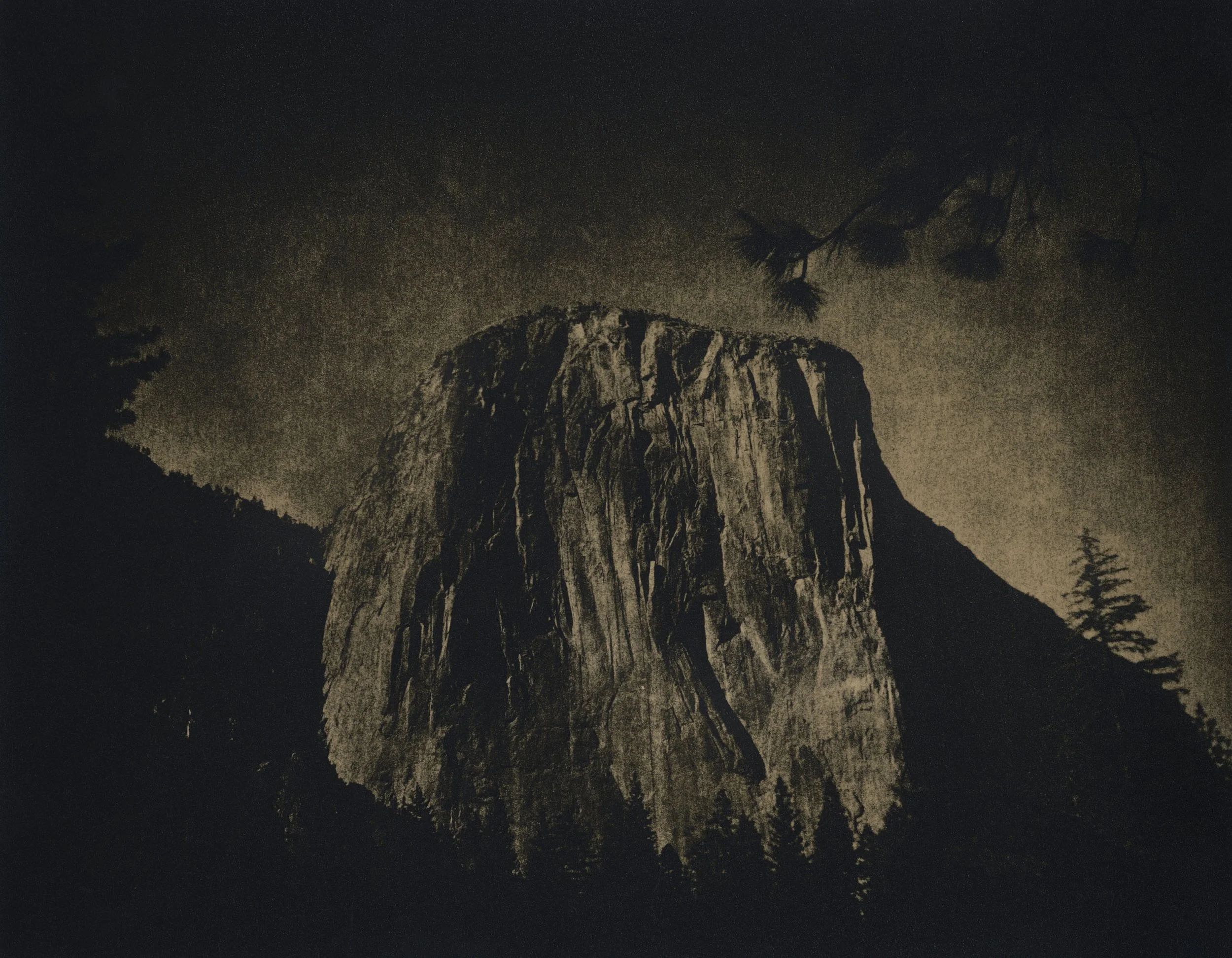 Nighttime view of a large granite monolith mountain with trees in the foreground and dark sky above.