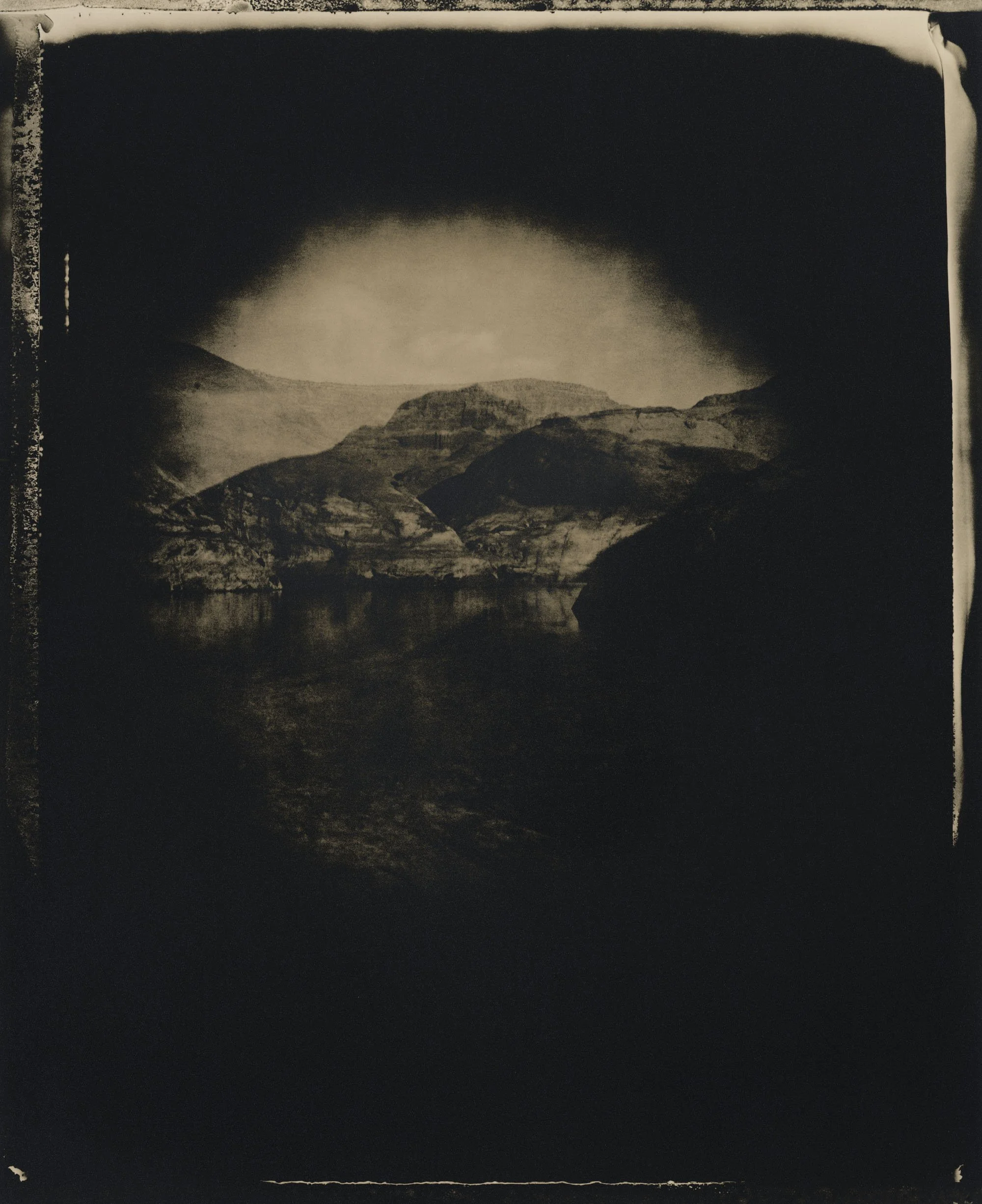 Black and white photograph of a landscape with mountains, a body of water, and a cloudy sky.