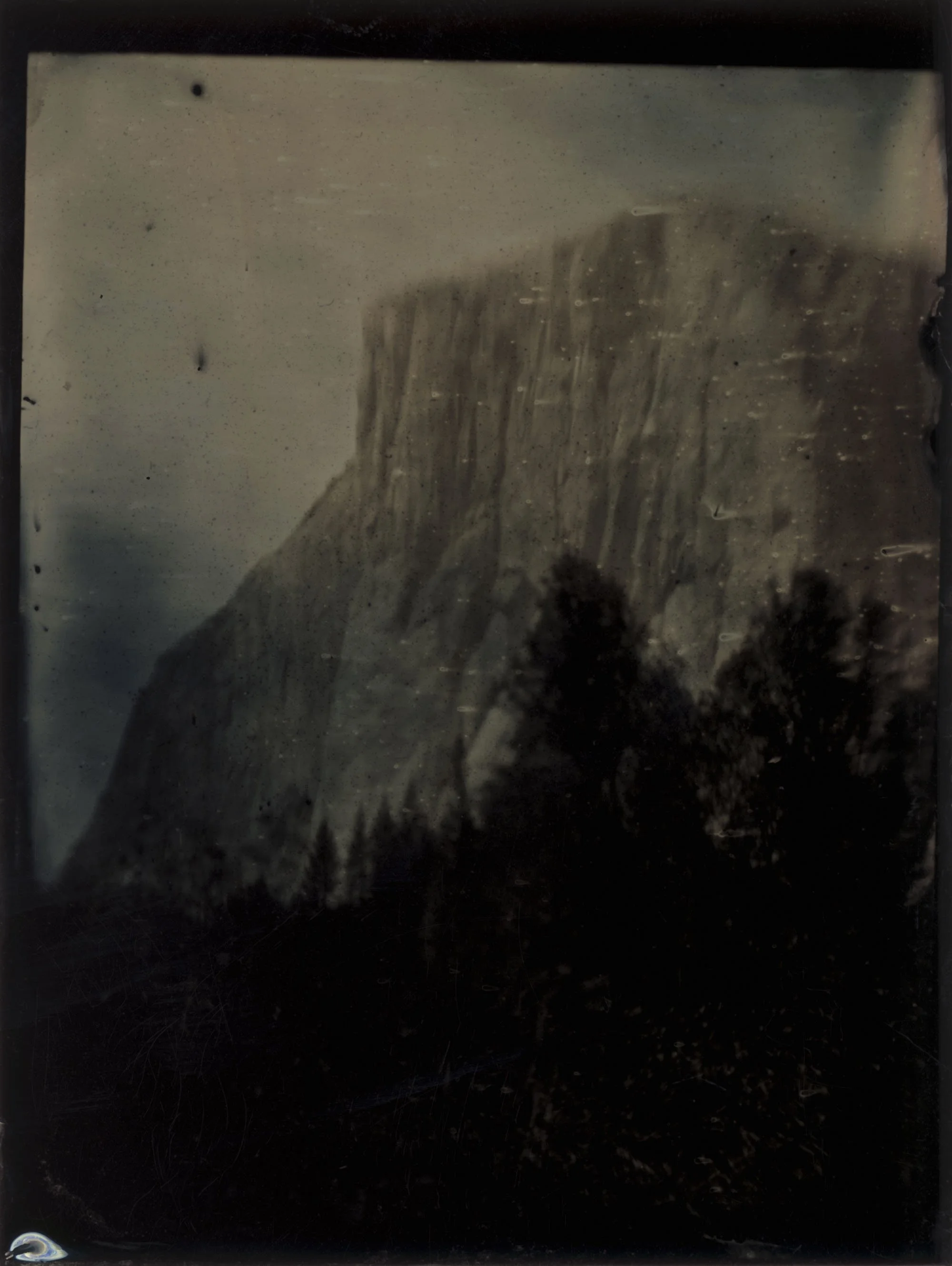Black and white photograph of a large mountain with trees in the foreground.