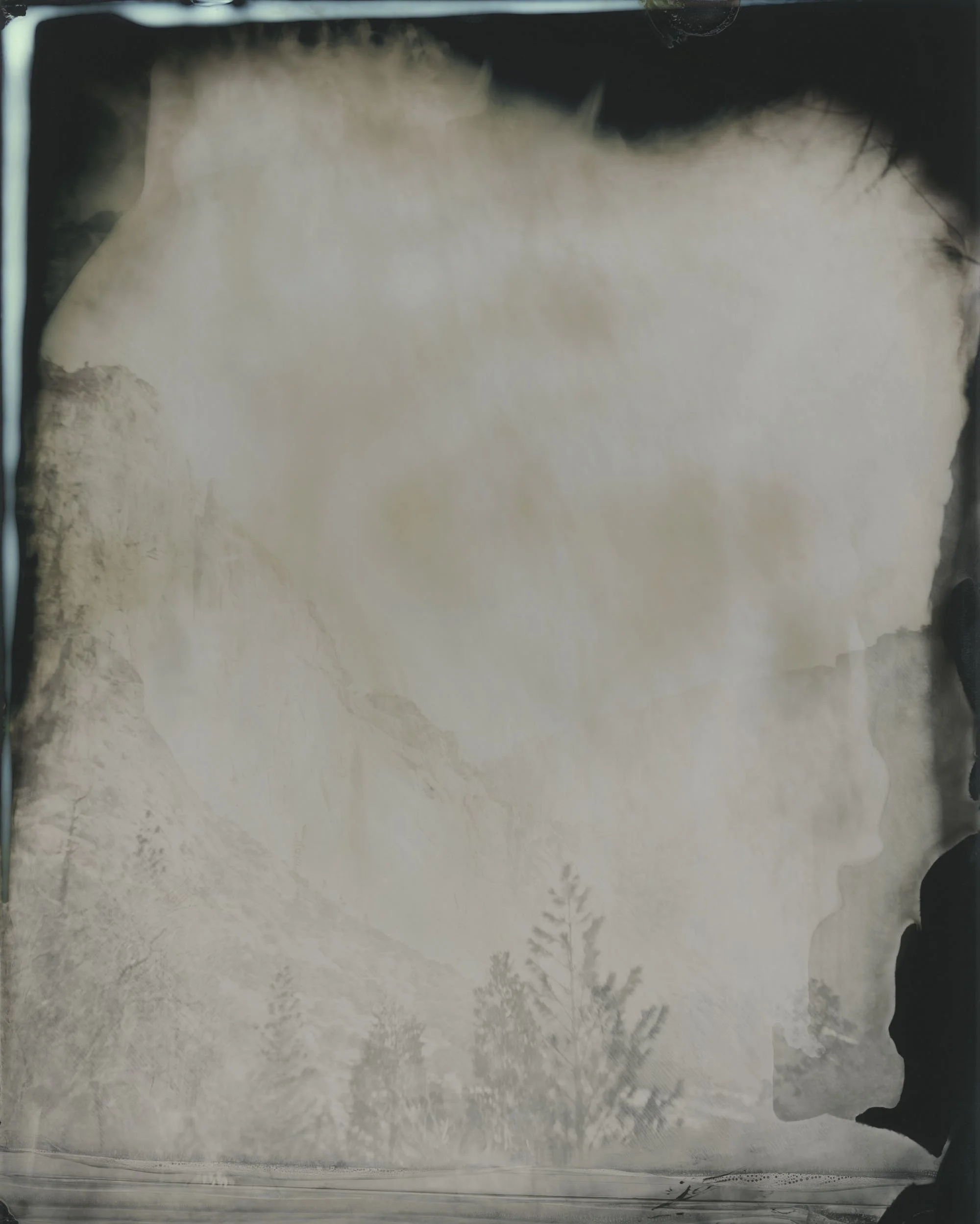 A foggy mountain landscape with trees, viewed through a glass window with some reflections and black borders.