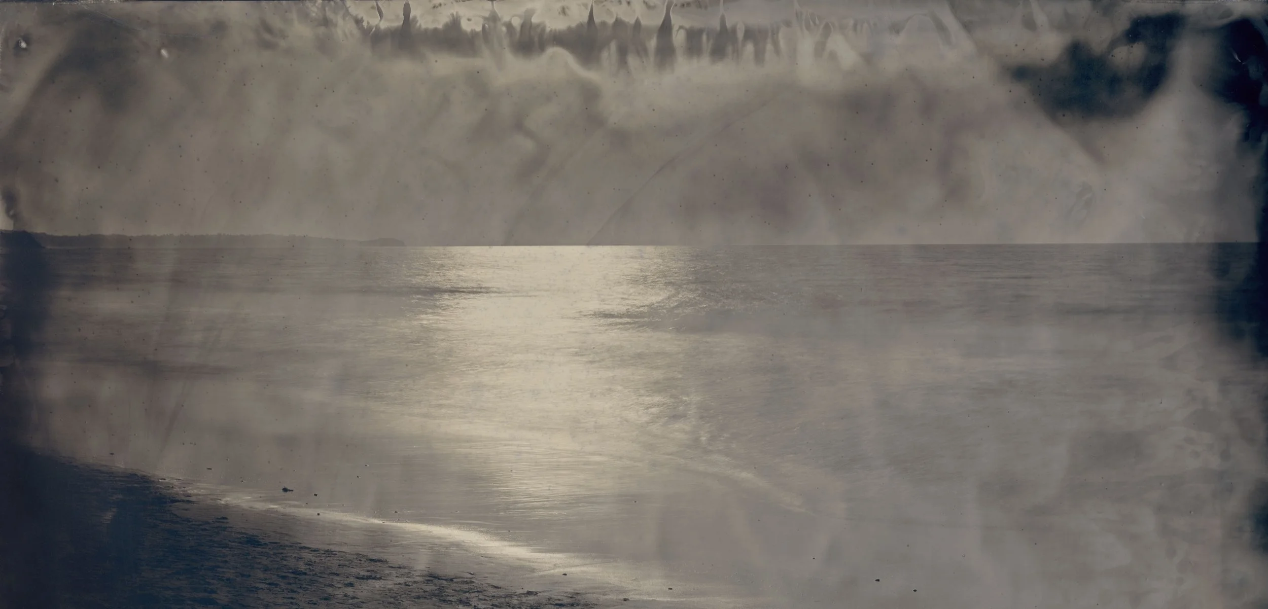 Black and white photo of ocean waves with cloudy sky and distant horizon
