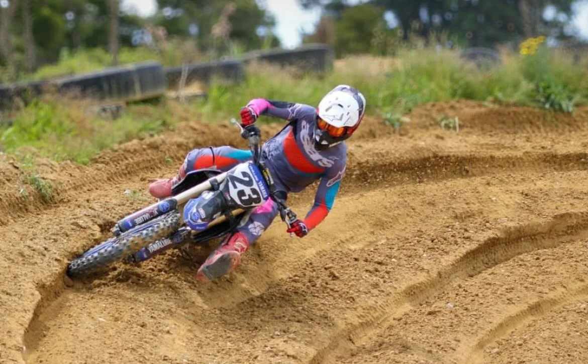 A person wearing a helmet and goggles riding a dirt bike on a curved dirt track outdoors.