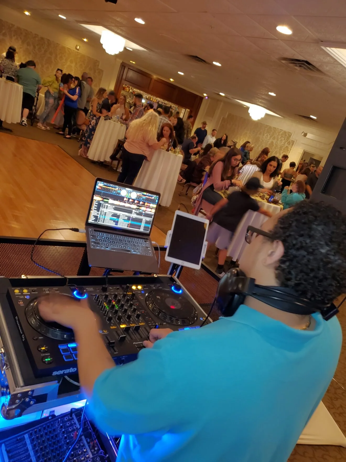 DJ performing at a wedding reception or party, with guests socializing in the background.