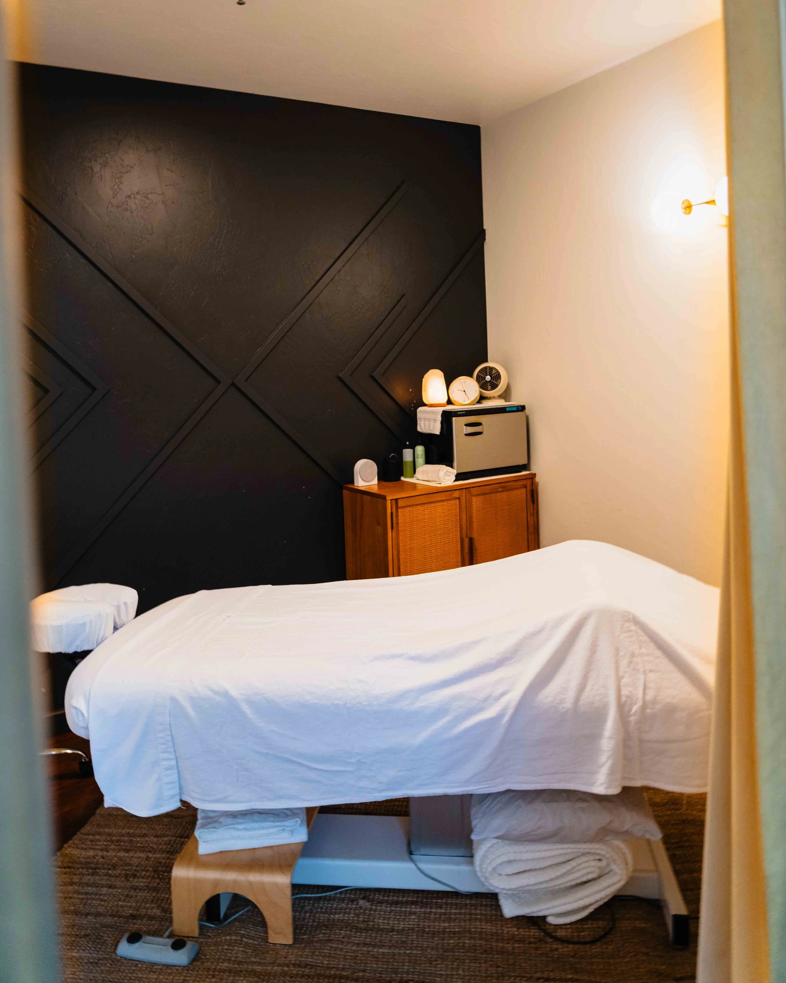 A hotel room with a bed, nightstand, and decorative items, viewed from the doorway.
