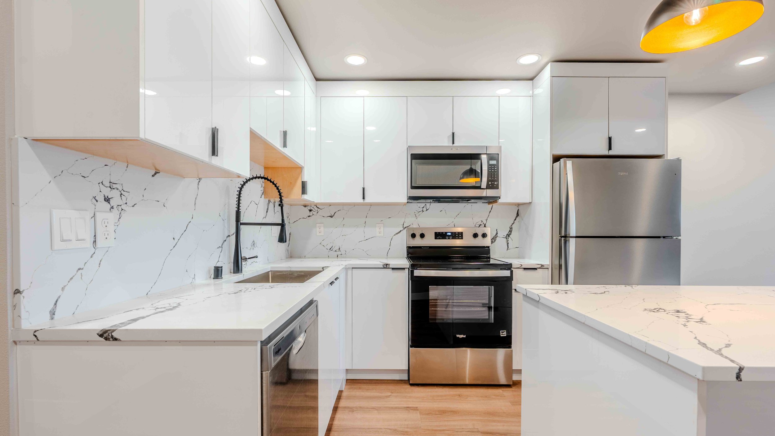 Modern kitchen with white cabinets, marble countertops, stainless steel appliances, and a black faucet.
