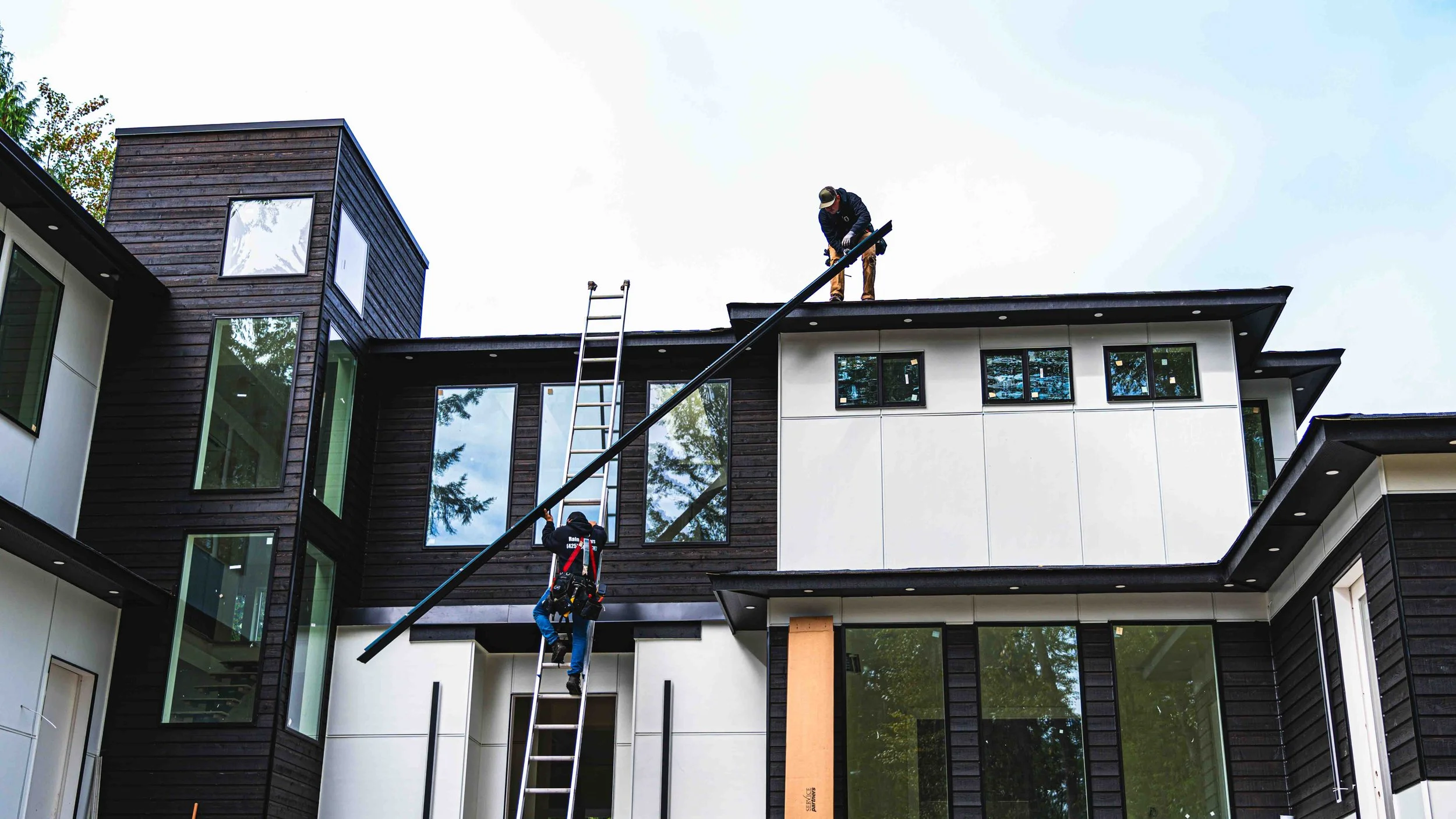 Workers installing a black security bar on the roof of a modern building with large windows.
