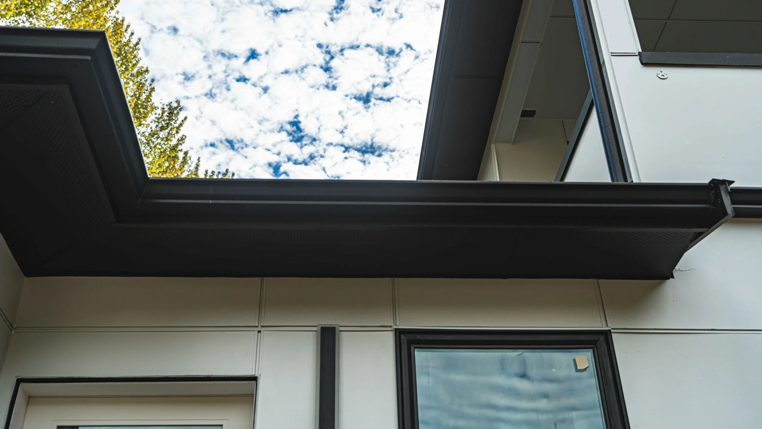 View through an open window showing a partly cloudy sky and part of a building's exterior with black trim.