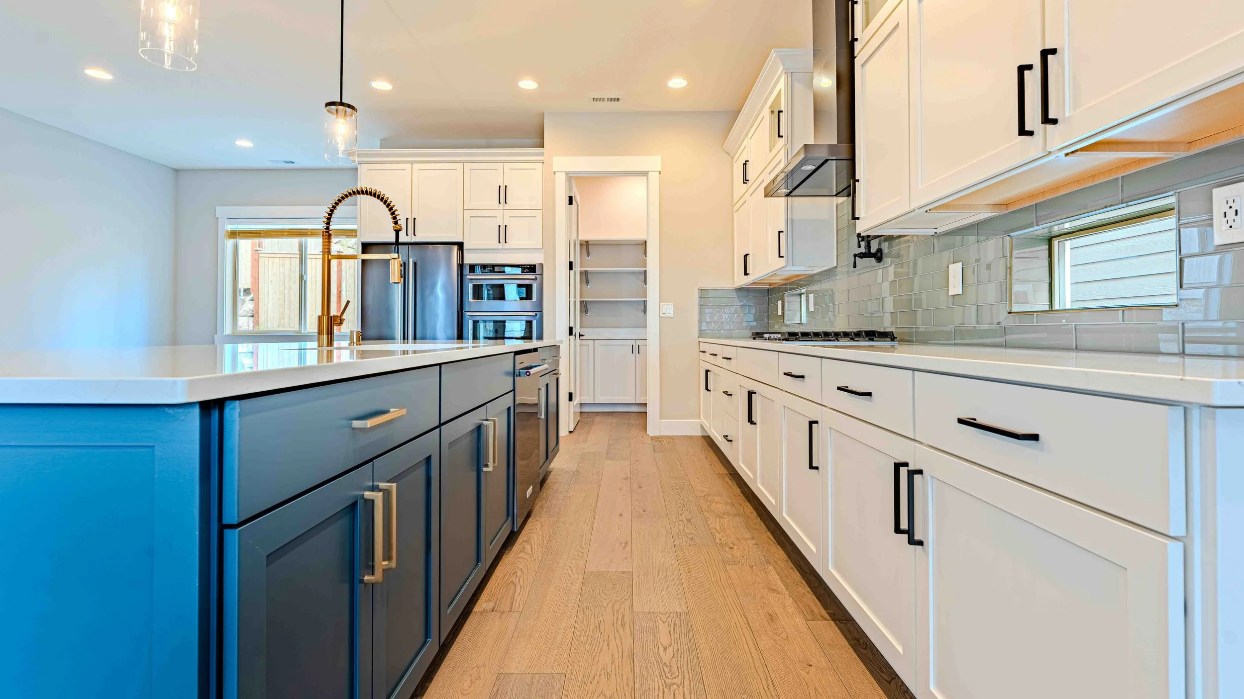 Modern kitchen with white cabinets, a blue island, hardwood floors, stainless steel appliances, and a tile backsplash.