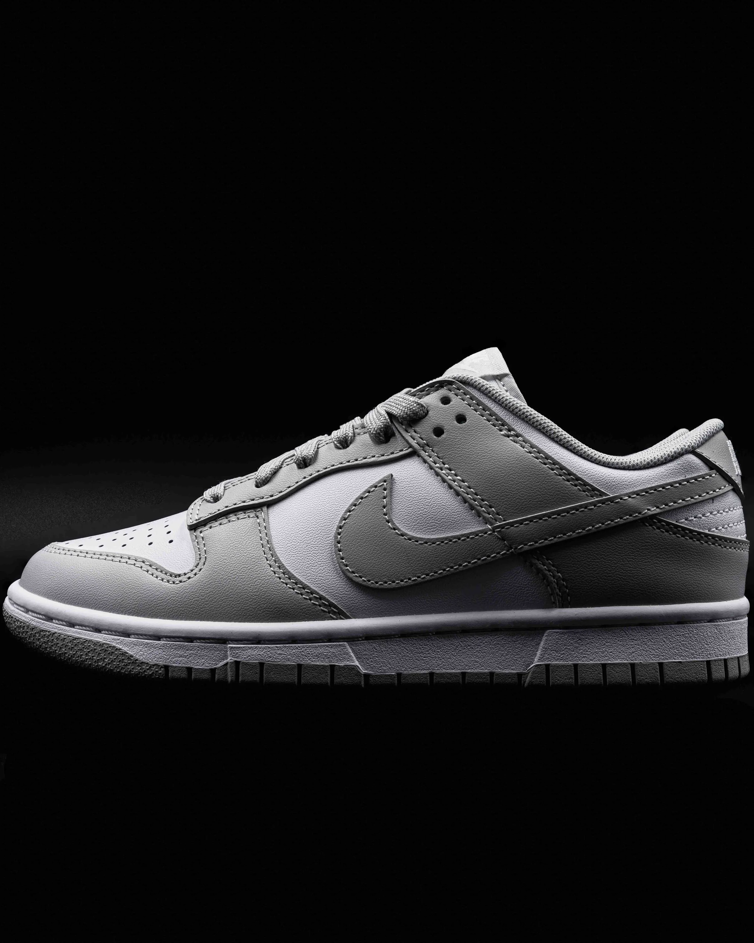 Close-up of a white athletic sneaker with gray accents, laces, and a thick sole, set against a black background.