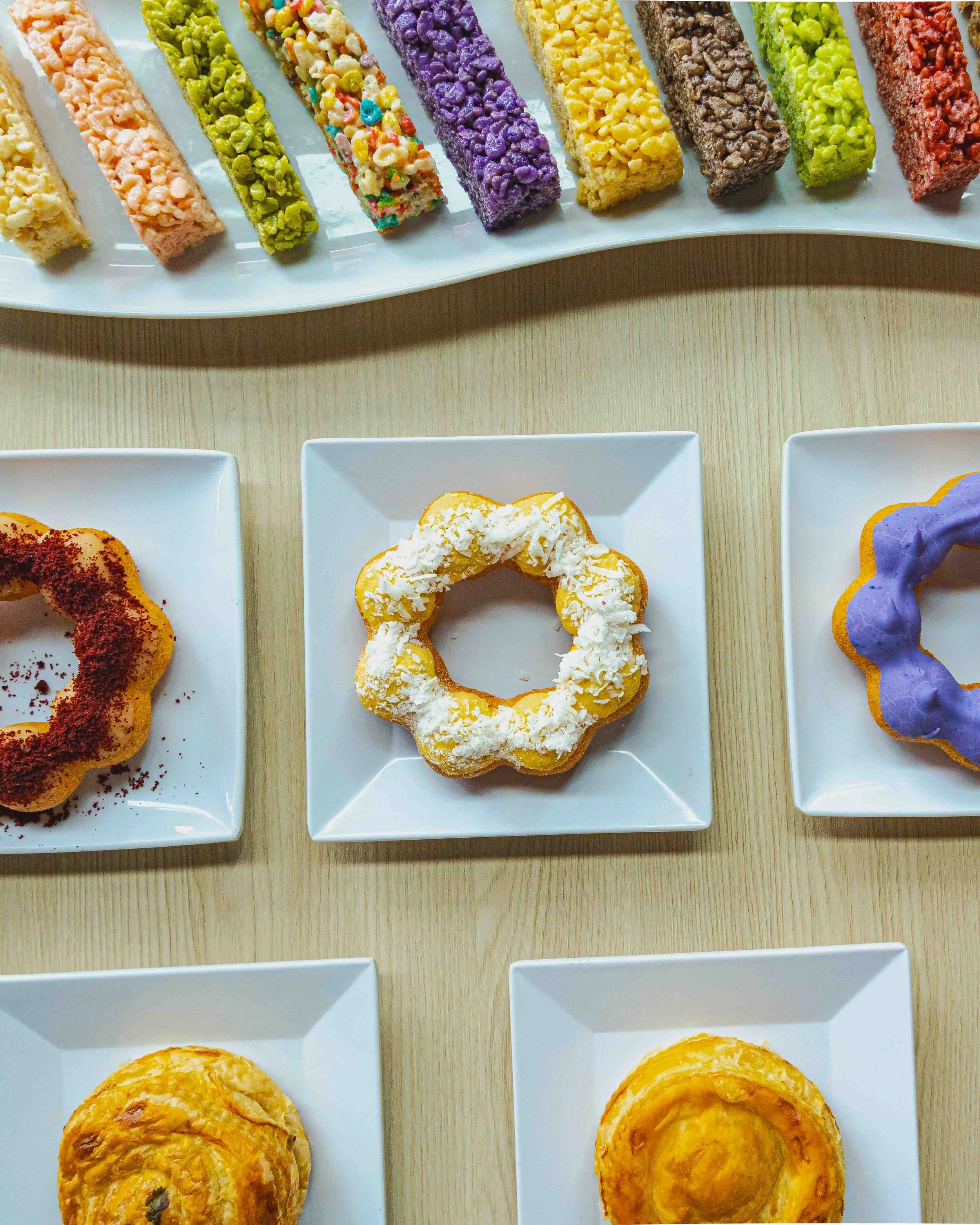 Colorful candy-colored rice krispie treats in various pastel shades topped with different sprinkles and candies, arranged on white serving plates.