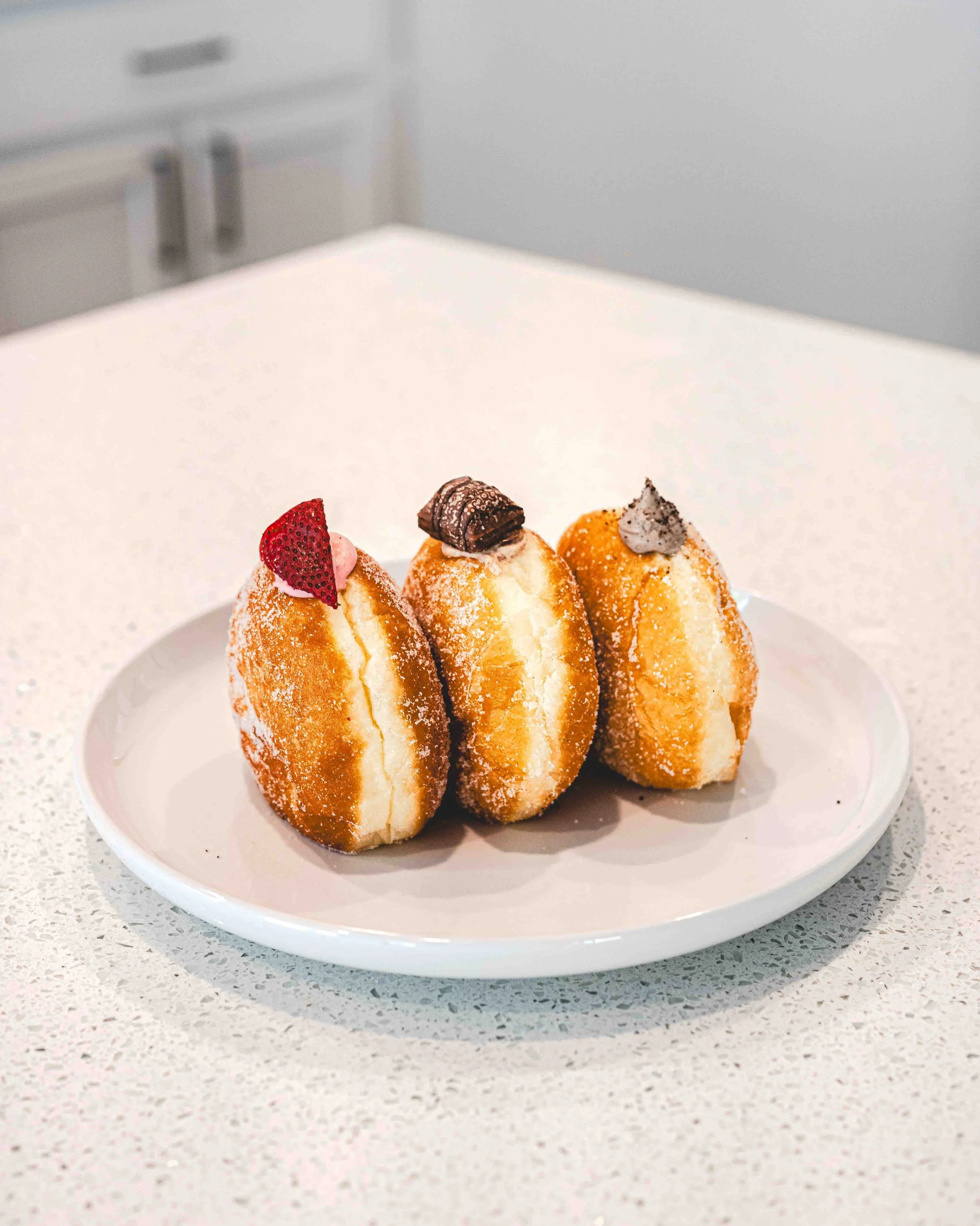 Three cannoli pastries with chocolate, fruit, and cream toppings on a white plate.