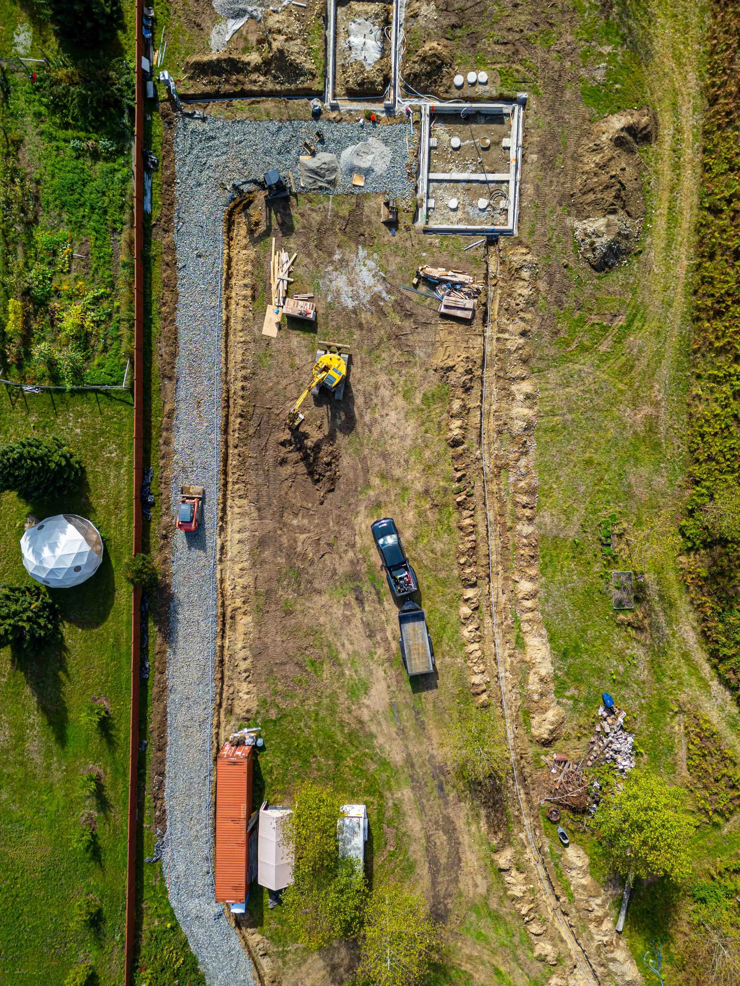 An aerial view of a construction site where a foundation is being prepared, with construction equipment, materials, and partially built structures visible.