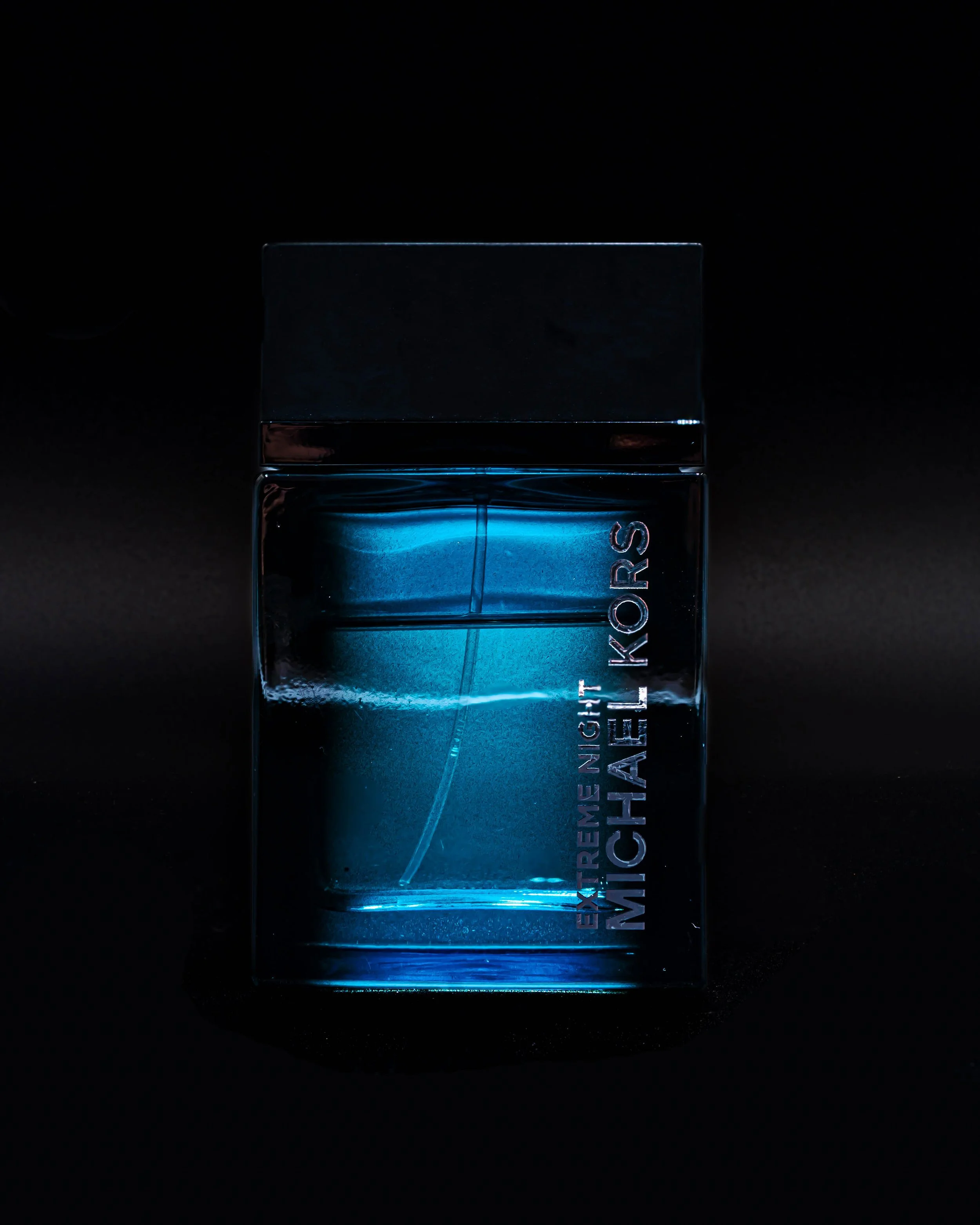 A glass perfume bottle with a black cap, illuminated with blue lighting, on a dark background.