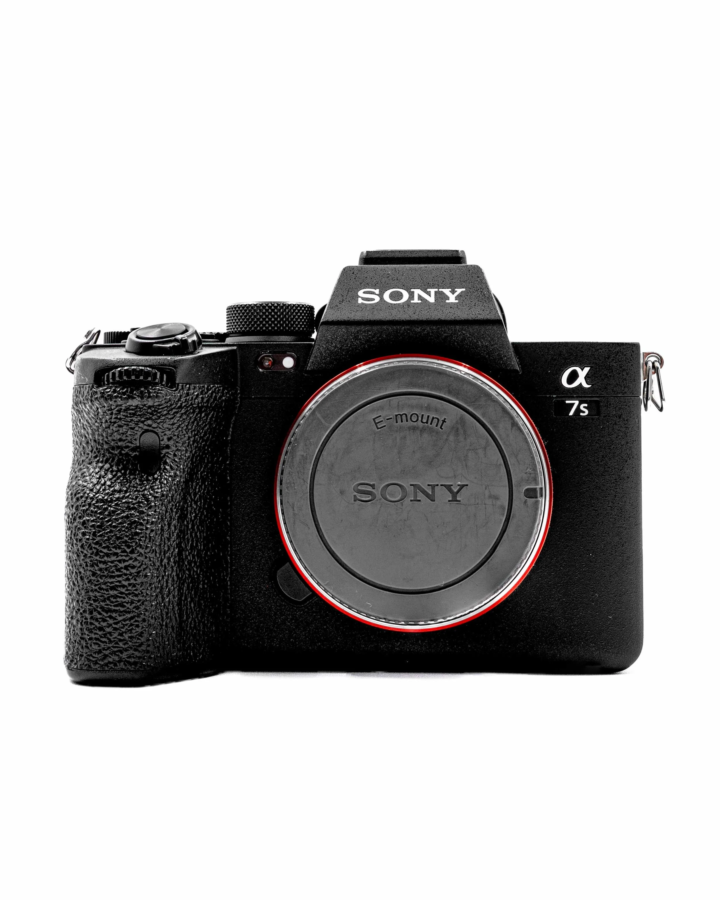 A black Sony mirrorless camera with a body grip, textured surface, and red ring around the lens mount, against a white background.