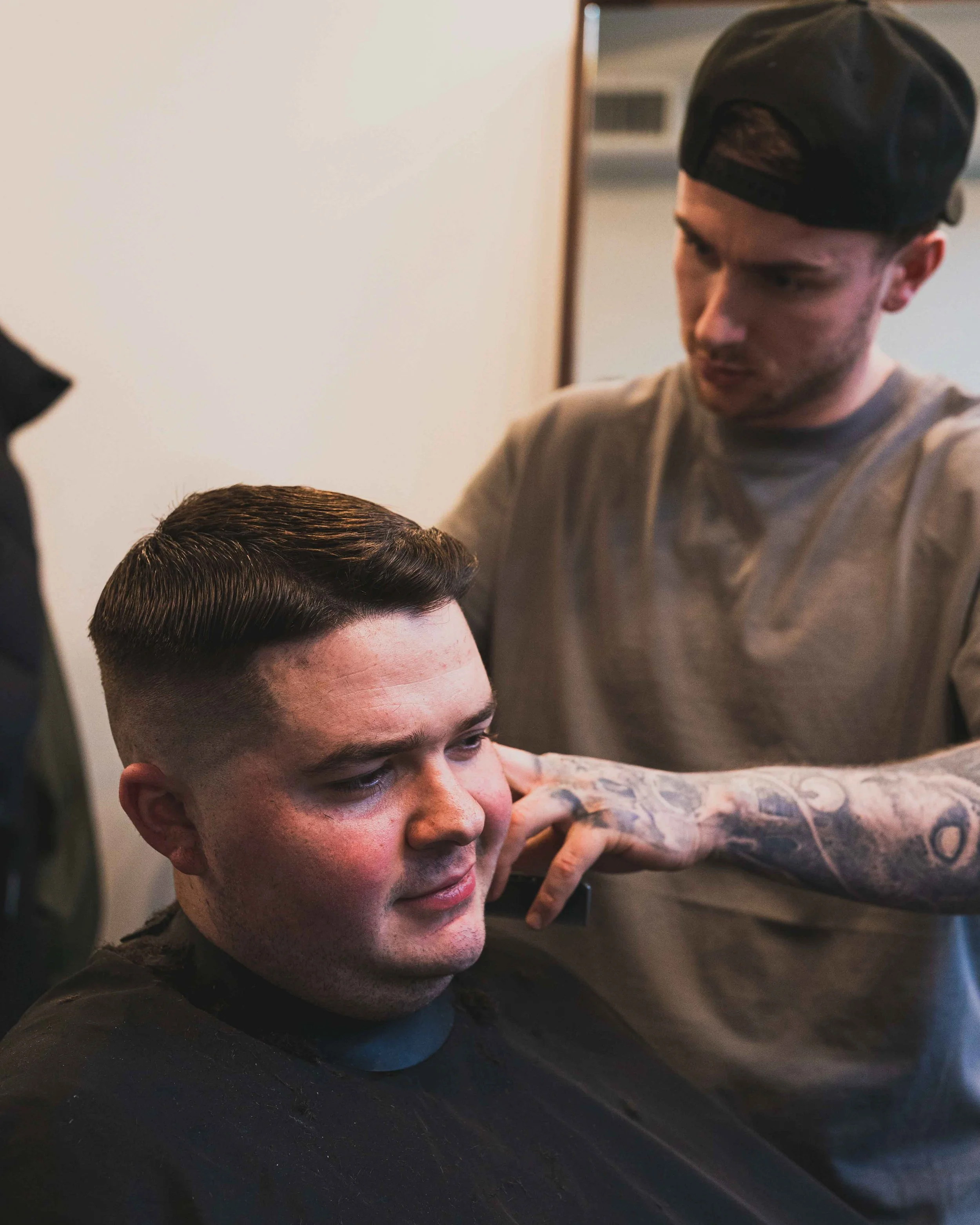 A young man with a fade haircut and a woman with tattooed arms in a tattoo studio.