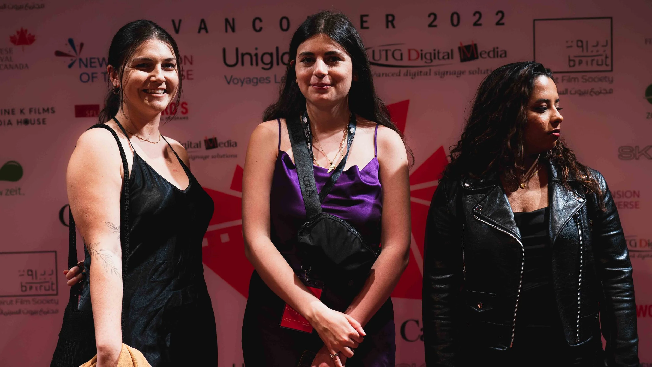 Three women standing in front of a pink backdrop with event and sponsor logos, smiling and posing for the photo.