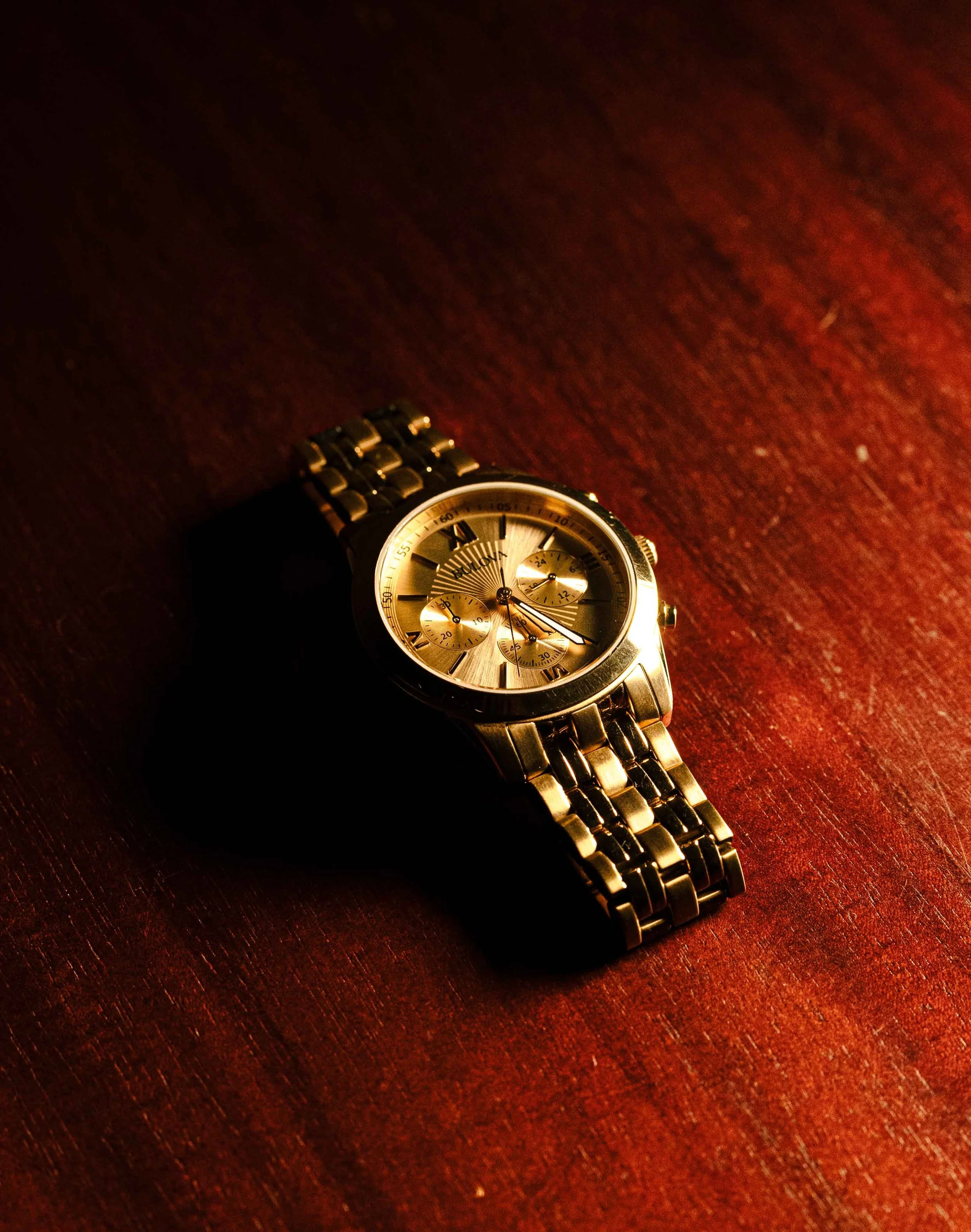 A gold-colored wristwatch with a metal band resting on a dark wooden surface.