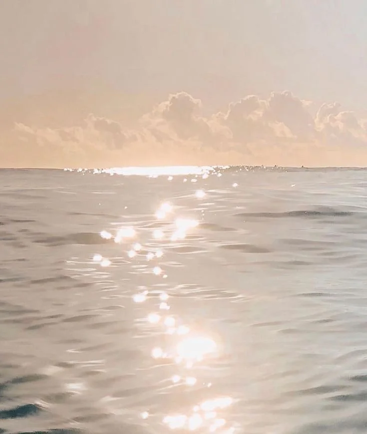 Sunset over the ocean with sunlight reflecting on the water and a few clouds in the sky.