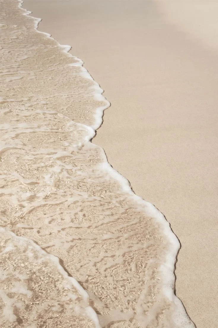 Photo of a sandy beach with gentle waves washing onto the shore.