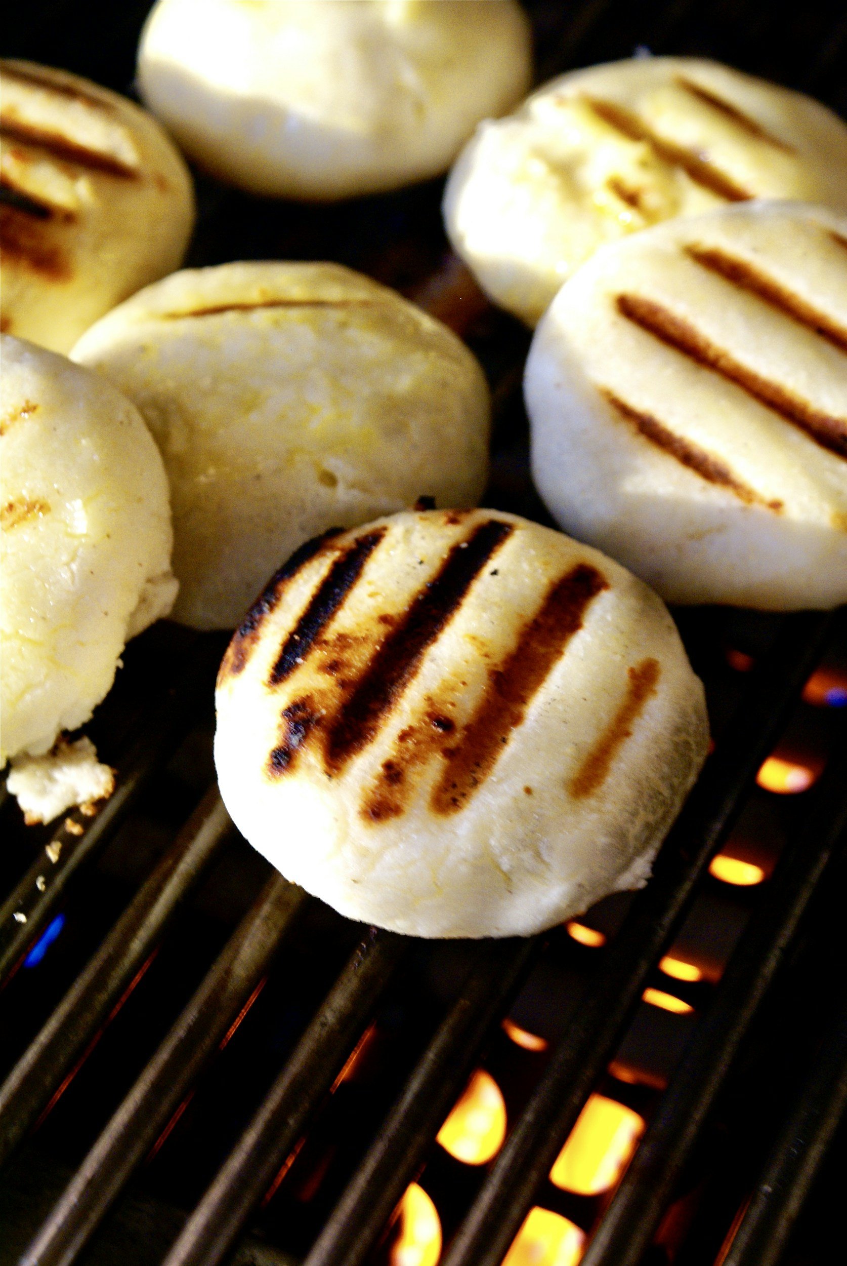 Image of white arepas cooking on a black grill.