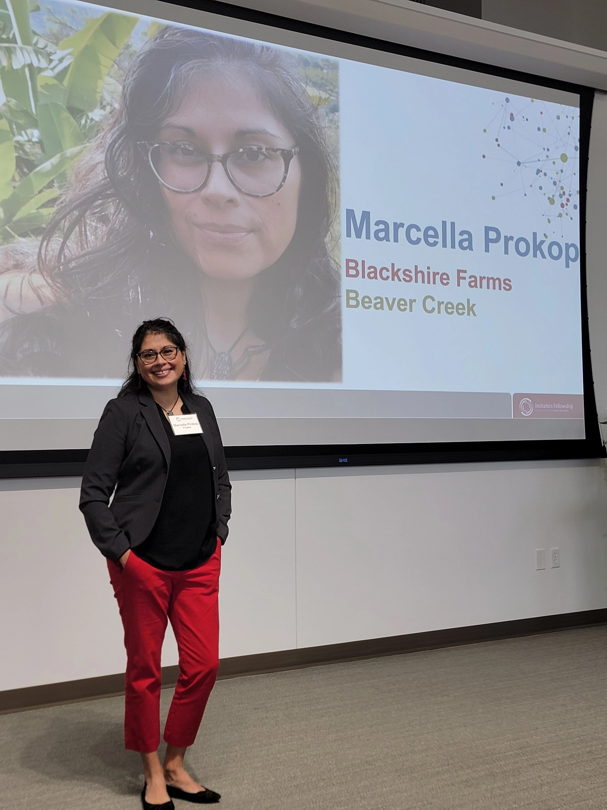 A woman with glasses,  red pants and a gray blazer smiles at the camera