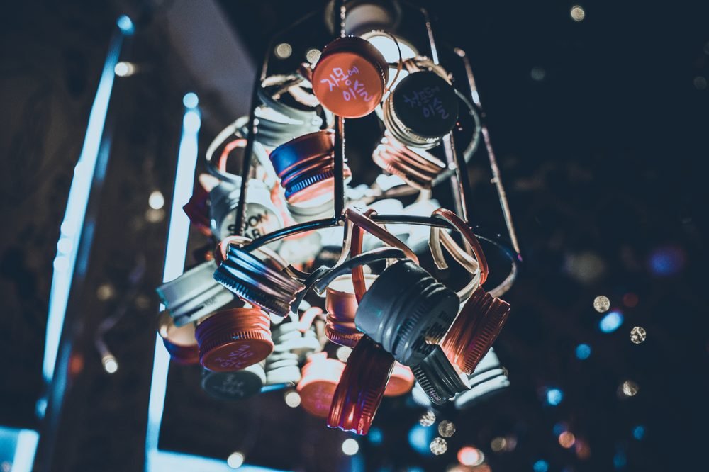 Chandelier made of assorted small jars and bottles hanging from chains in a dark room.
