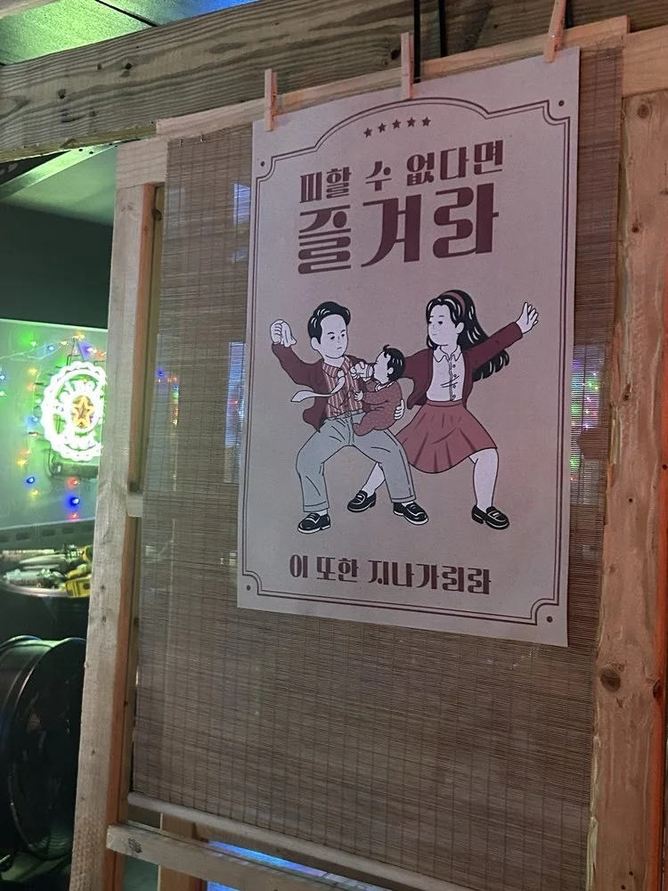 A sign with Korean text and illustration of a family fighting, with a man pulling a woman's hair and a girl standing with arms outstretched.