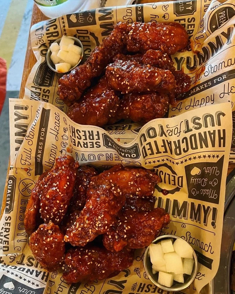 Two servings of glazed chicken wings topped with sesame seeds, served with small containers of pickled radish.
