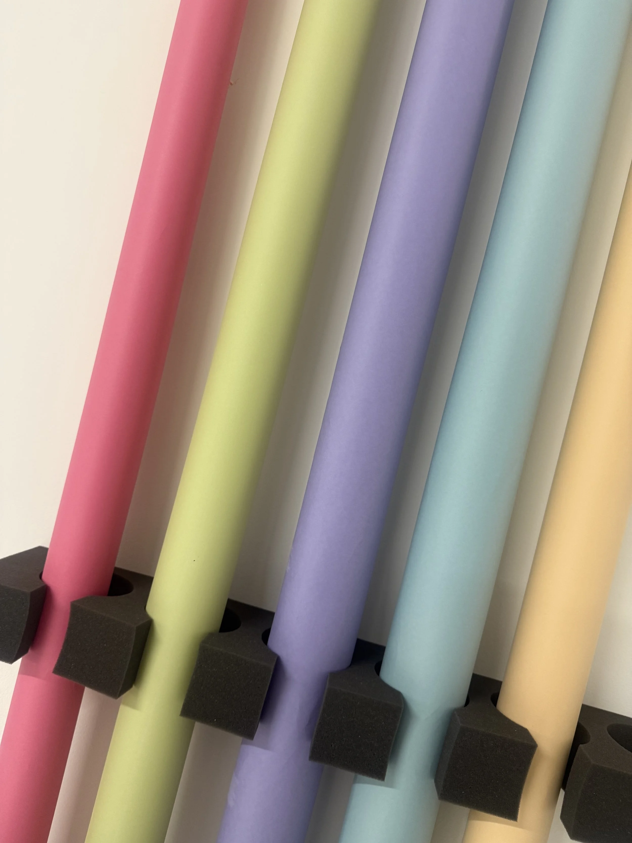 Colorful rolls of paper in pink, yellow, purple, blue, and cream held in black foam holders.