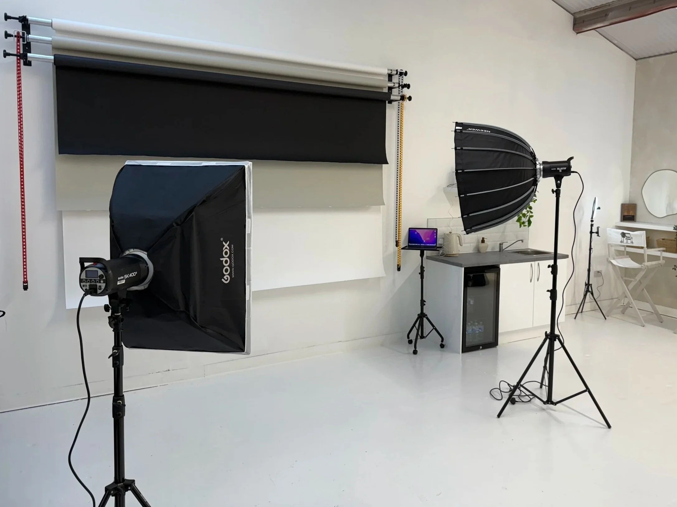 Photography studio with professional lighting equipment, green screen backdrop, and small kitchen area.