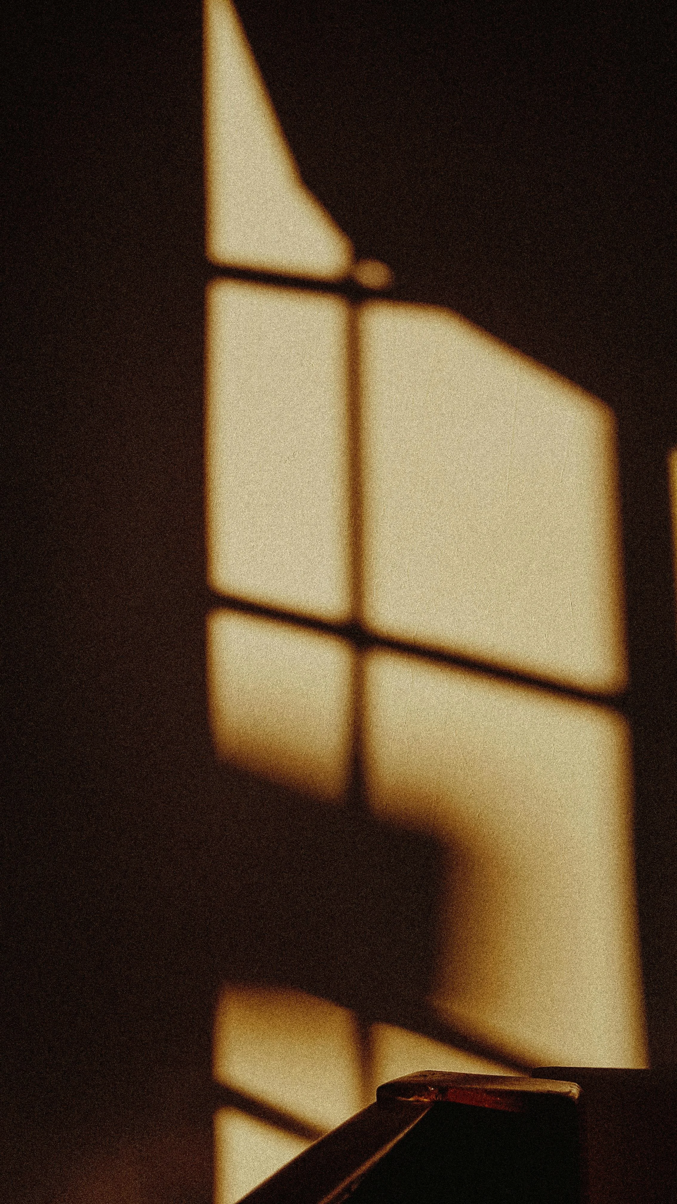 Sunlight casting shadow of a window with a grid pattern onto a wall and objects.