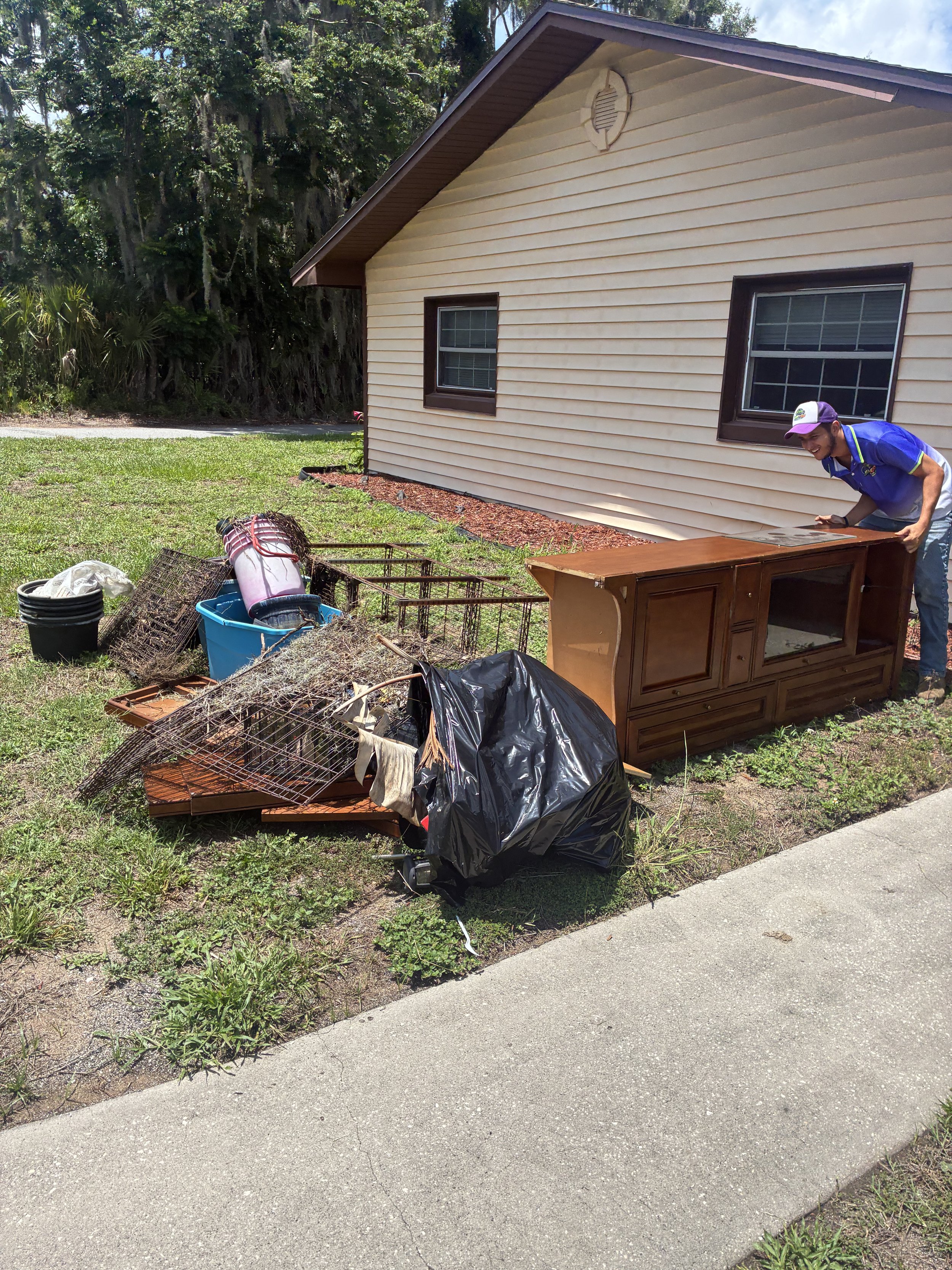 A man loading furniture onto a trailer attached to a silver SUV in a residential neighborhood with trees and houses in the background.