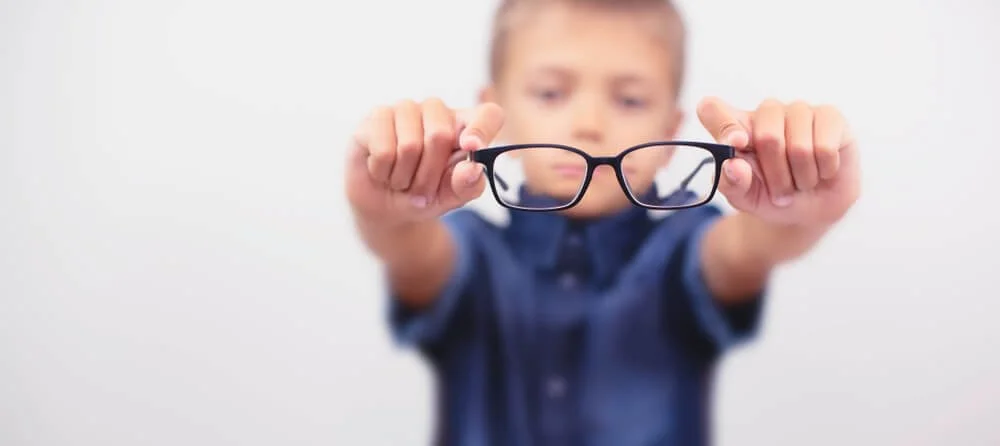 image of a child holding u pa pair of glasses that is clear and he is blurry behind them