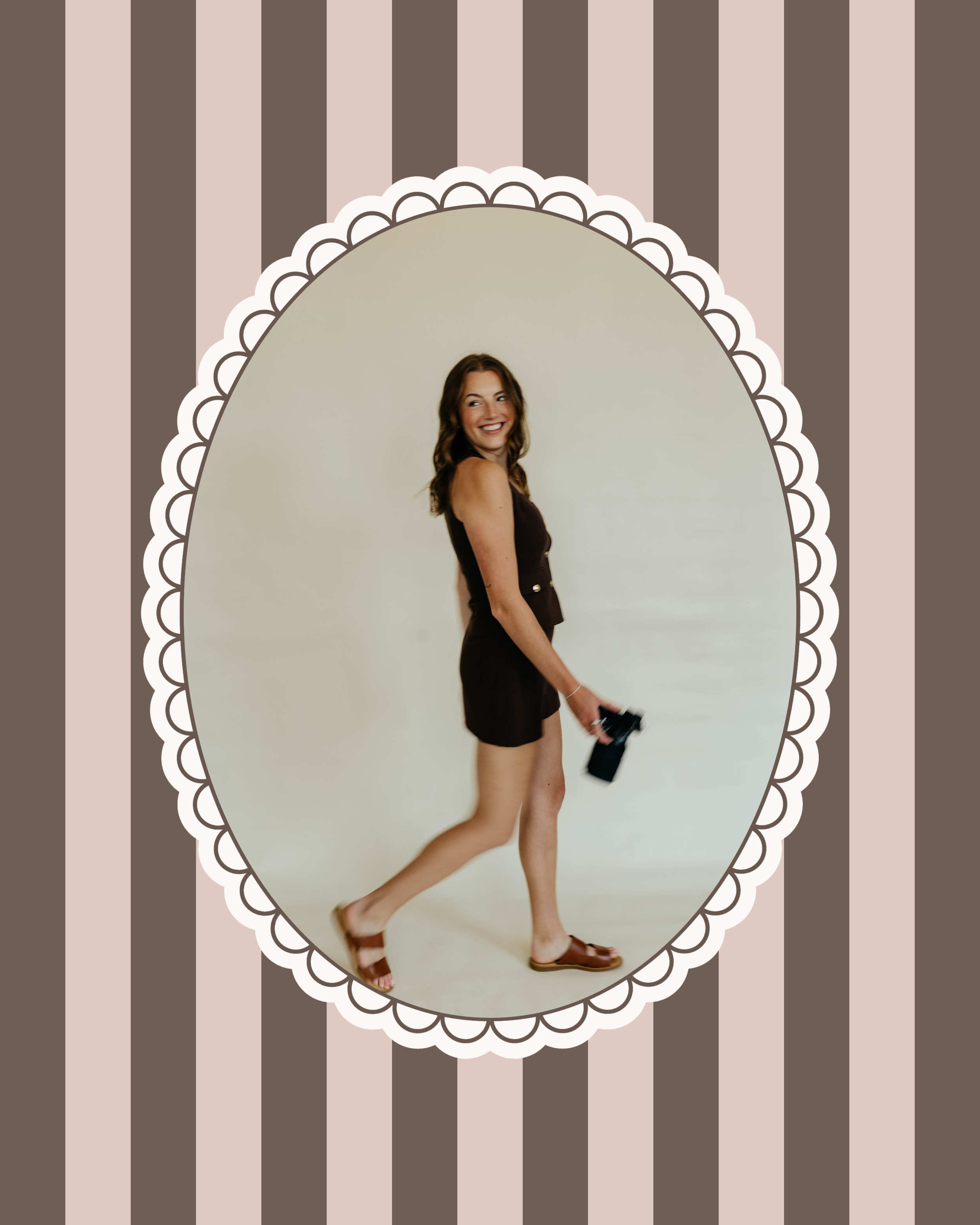 Young woman smiling and walking while holding a camera, dressed in a black sleeveless top, black shorts, and brown sandals, reflected in an ornate oval mirror with a striped background.