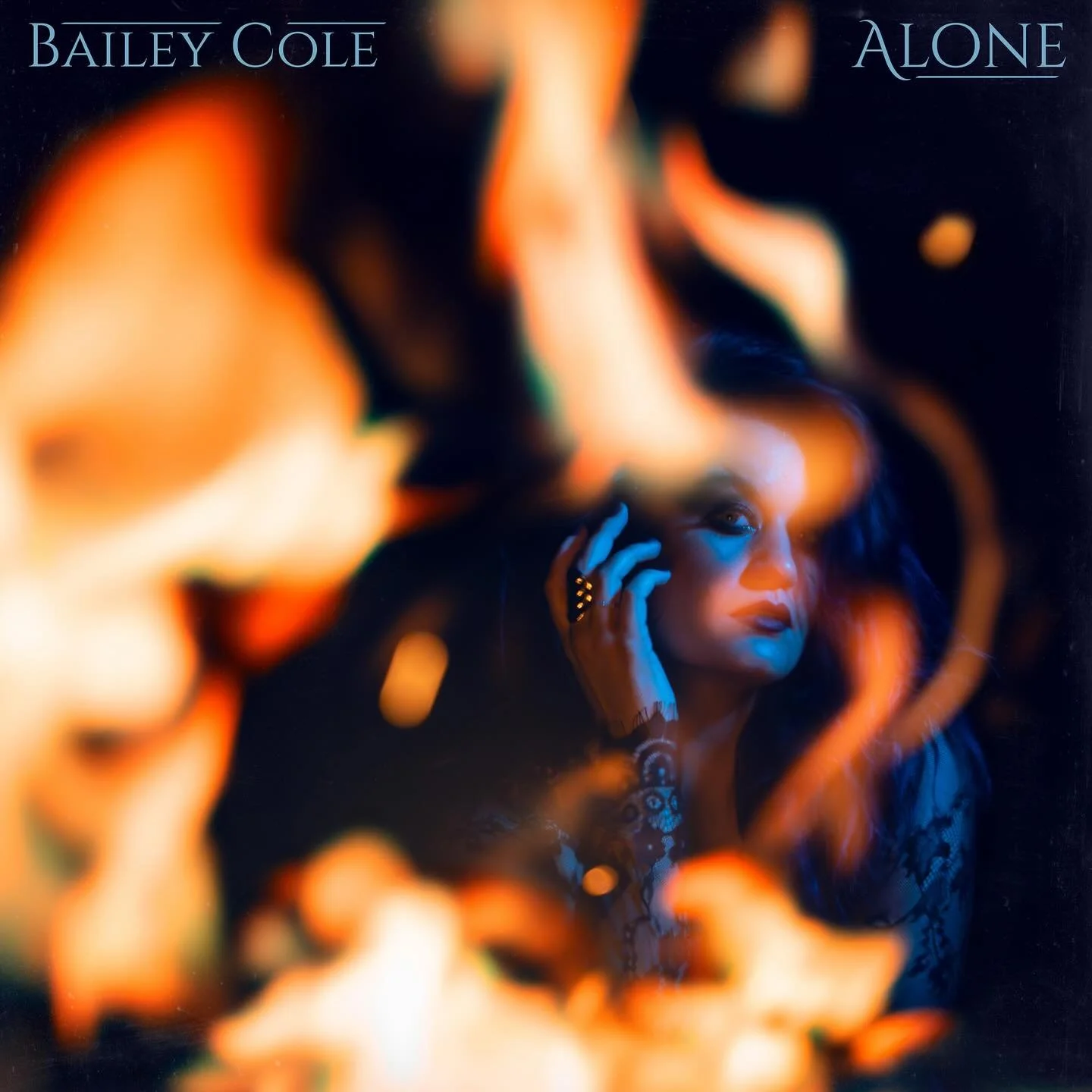 An album cover for Bailey Cole's 'Alone,' featuring a woman with makeup and jewelry, framed by swirling orange and blue flames or smoke.