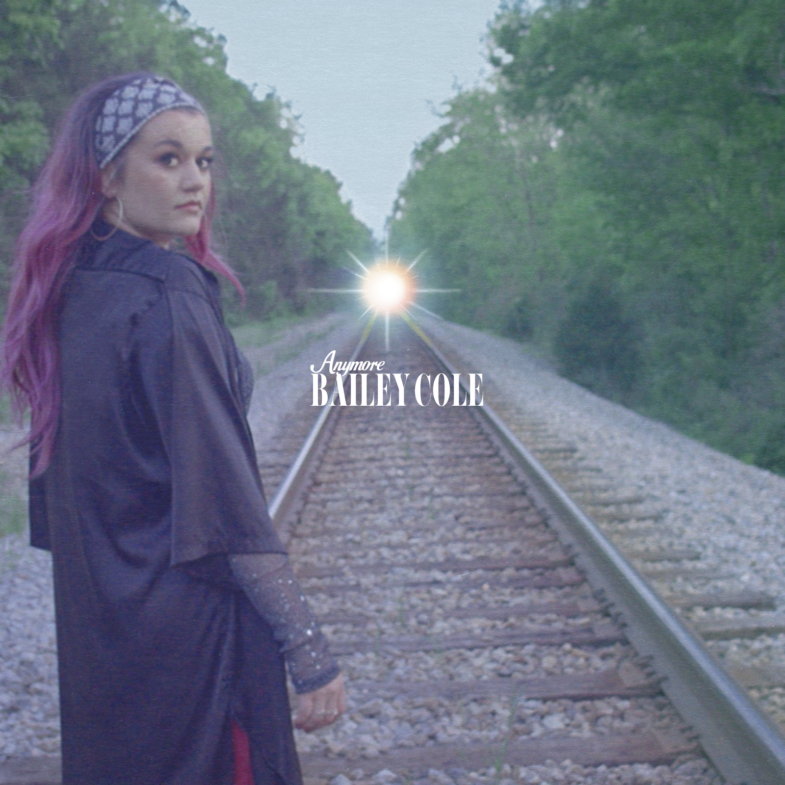 A woman with purple hair and a headband standing on railroad tracks, looking over her shoulder with trees in the background, with a bright light and the text 'No More Bailey Cole' overlayed on the image.