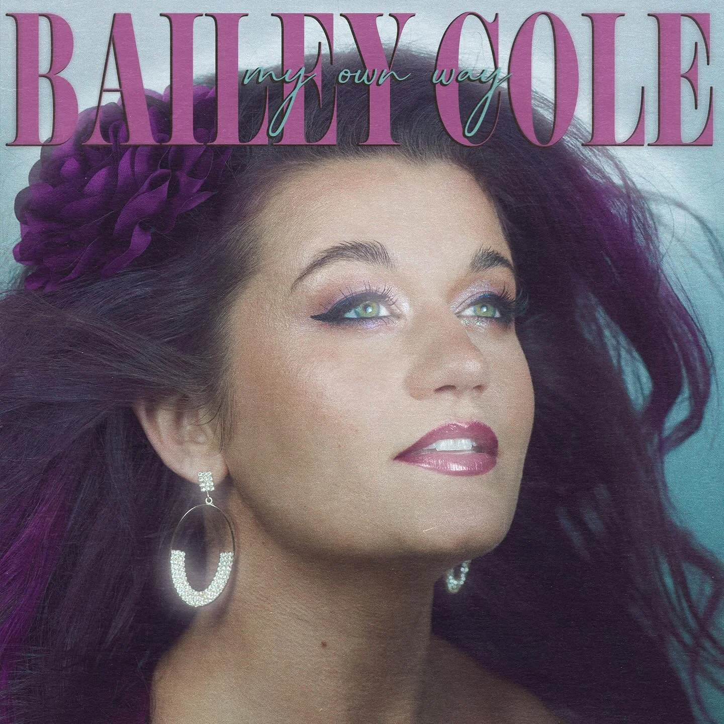 Close-up of a woman with dark flowing hair, hoop earrings, and makeup with pink lipstick and winged eyeliner, on the cover of a magazine titled 'Baldy Cole my own way'.