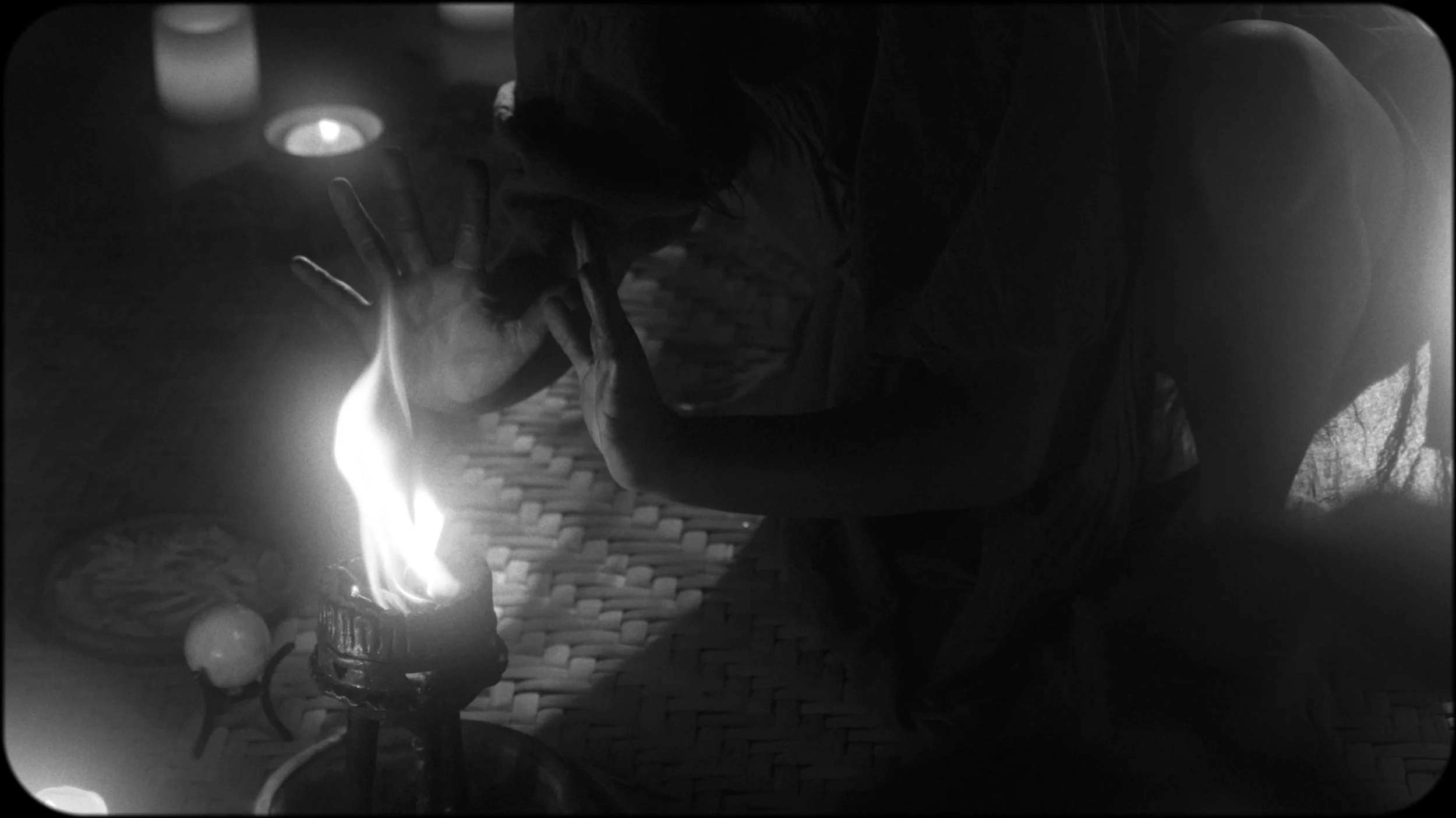 Person leaning over a table, blowing out candles on a birthday cake, with lit candles and a candle in the background, in black and white.
