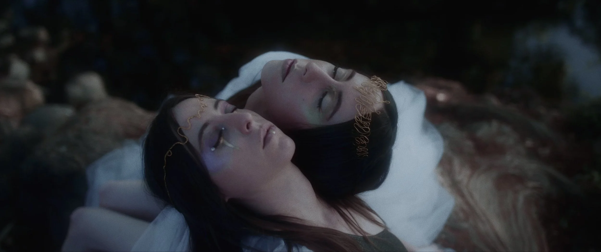 Two women with closed eyes lying in a shallow pool of water surrounded by rocks at night