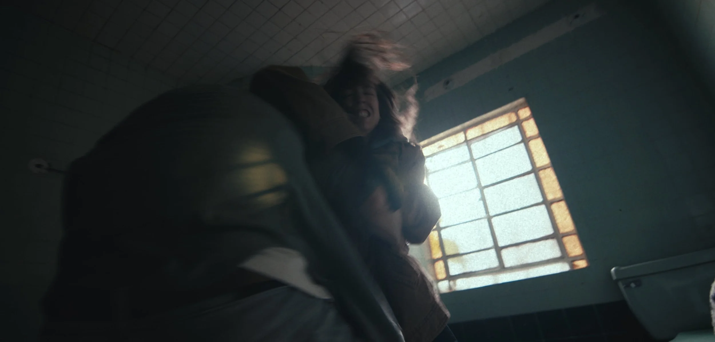 A woman with curly hair and a woman with straight hair engaged in a fight in a dimly lit room with a stained glass window.