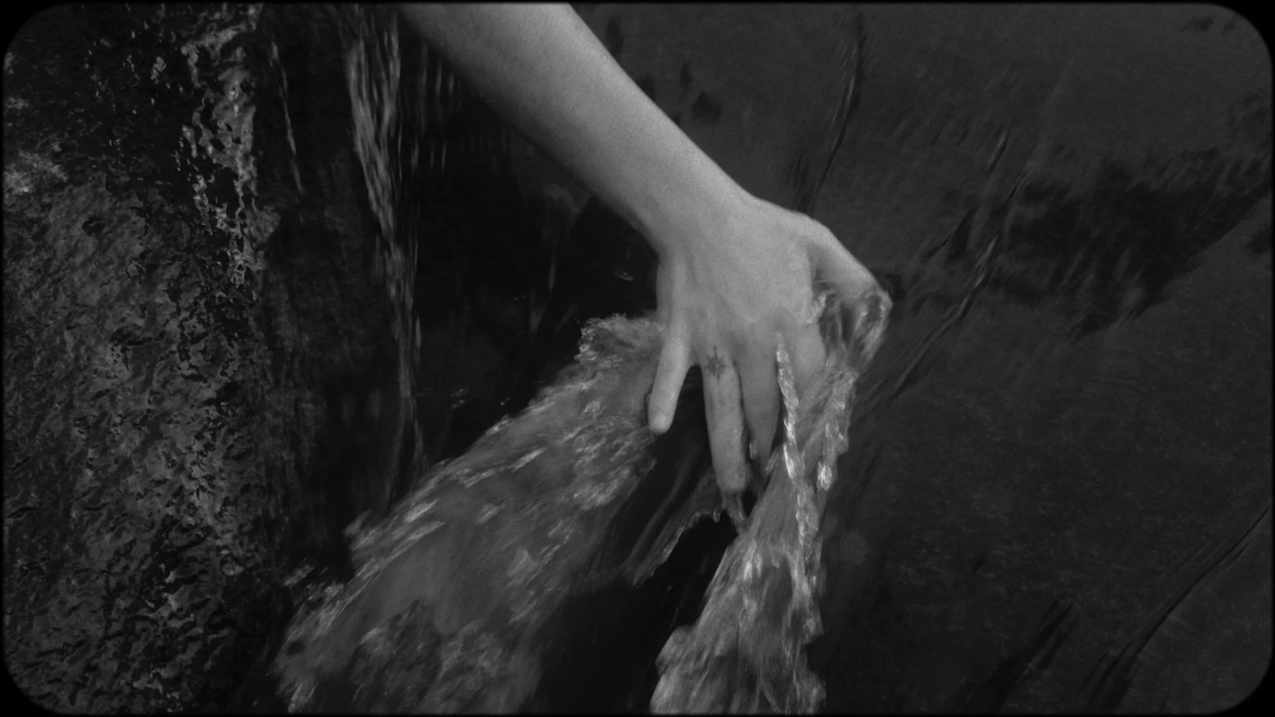 A person's hand moving through running water in a dark environment, possibly a wooden or stone surface.