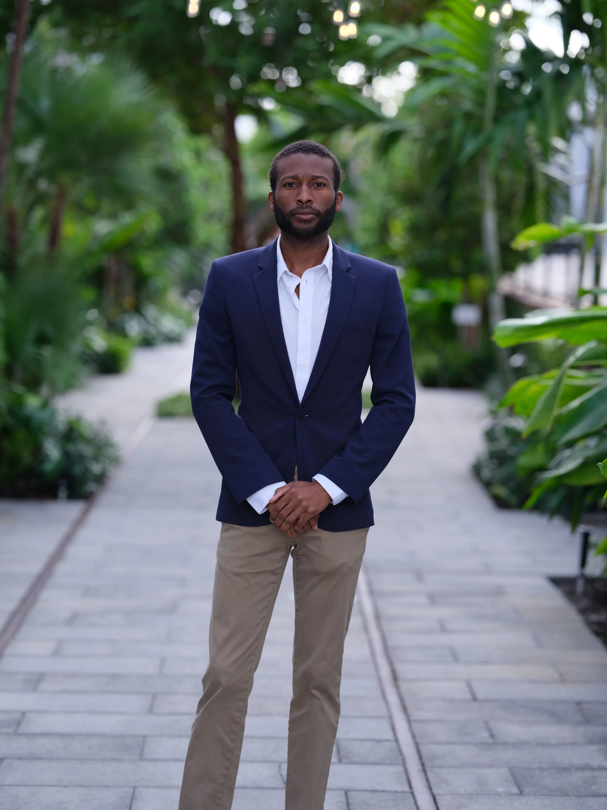 Roger Jackson  standing outdoors on a paved path surrounded by lush green plants.