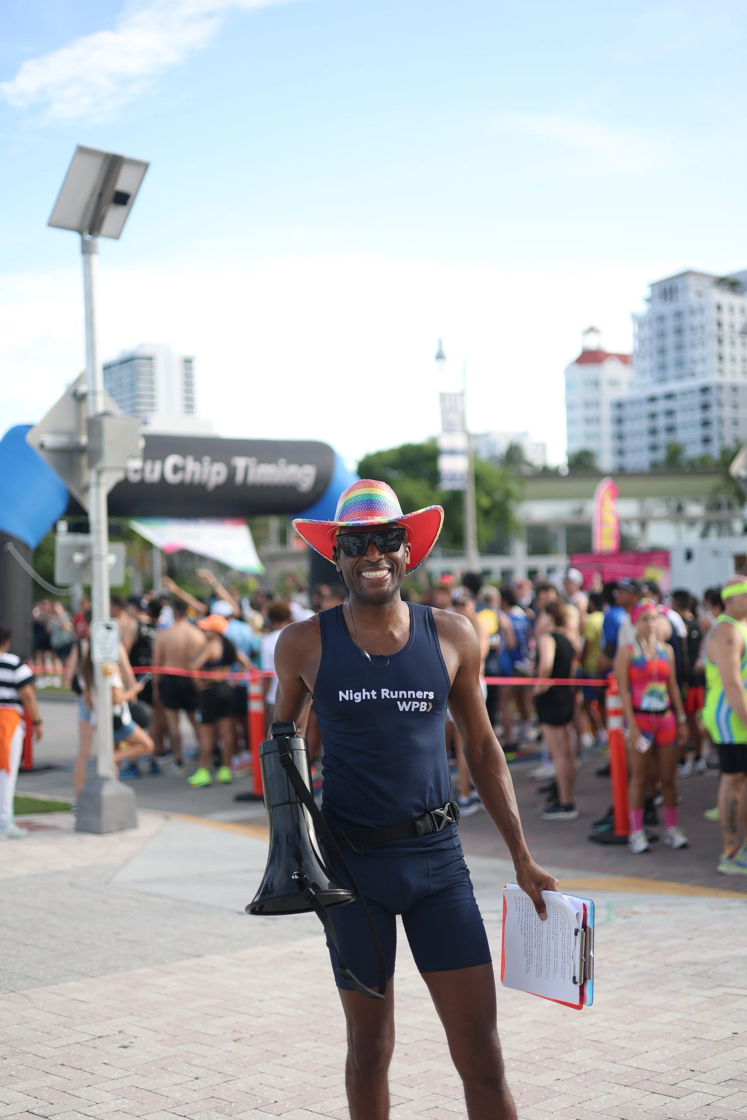 Roger Jackson  holding a clipboard and a megaphone, with a crowd of runners and city buildings in the background.