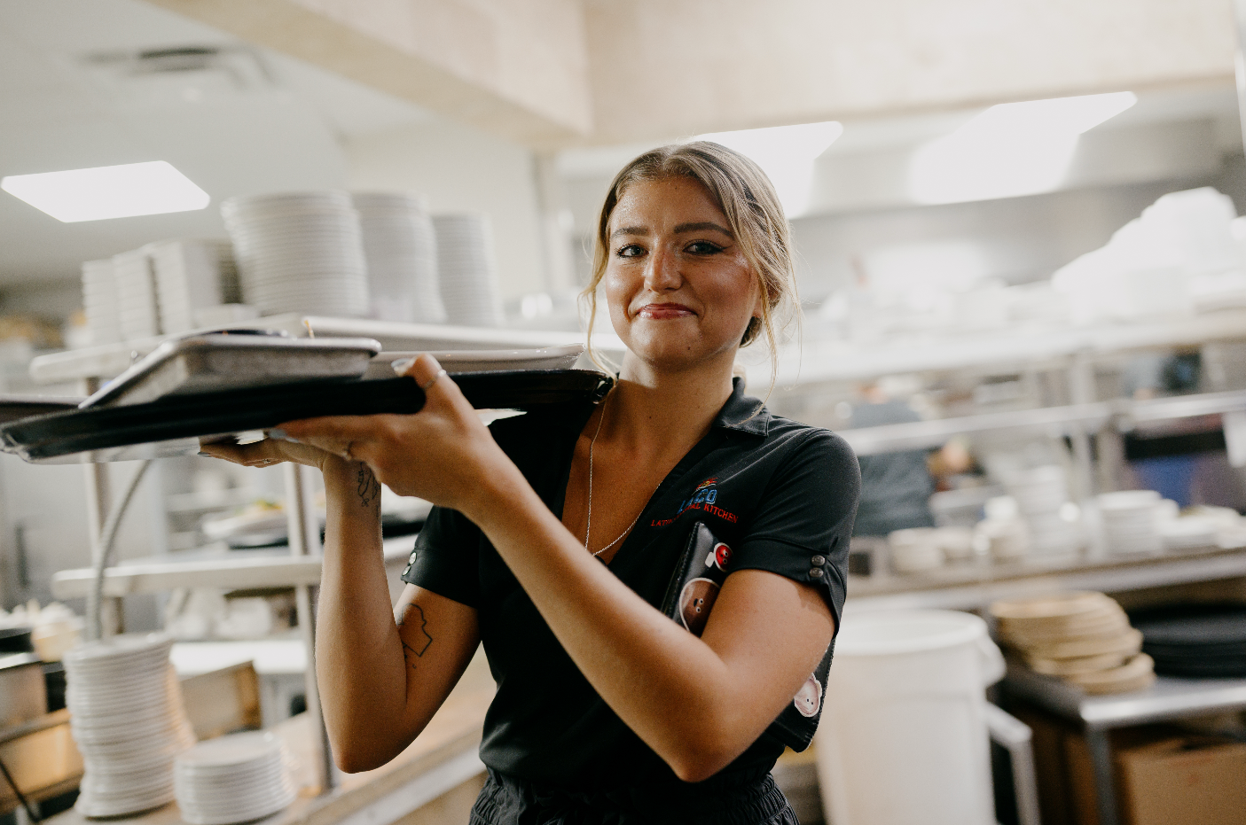 Female restaurant worker holding a tray with plates in a kitchen.