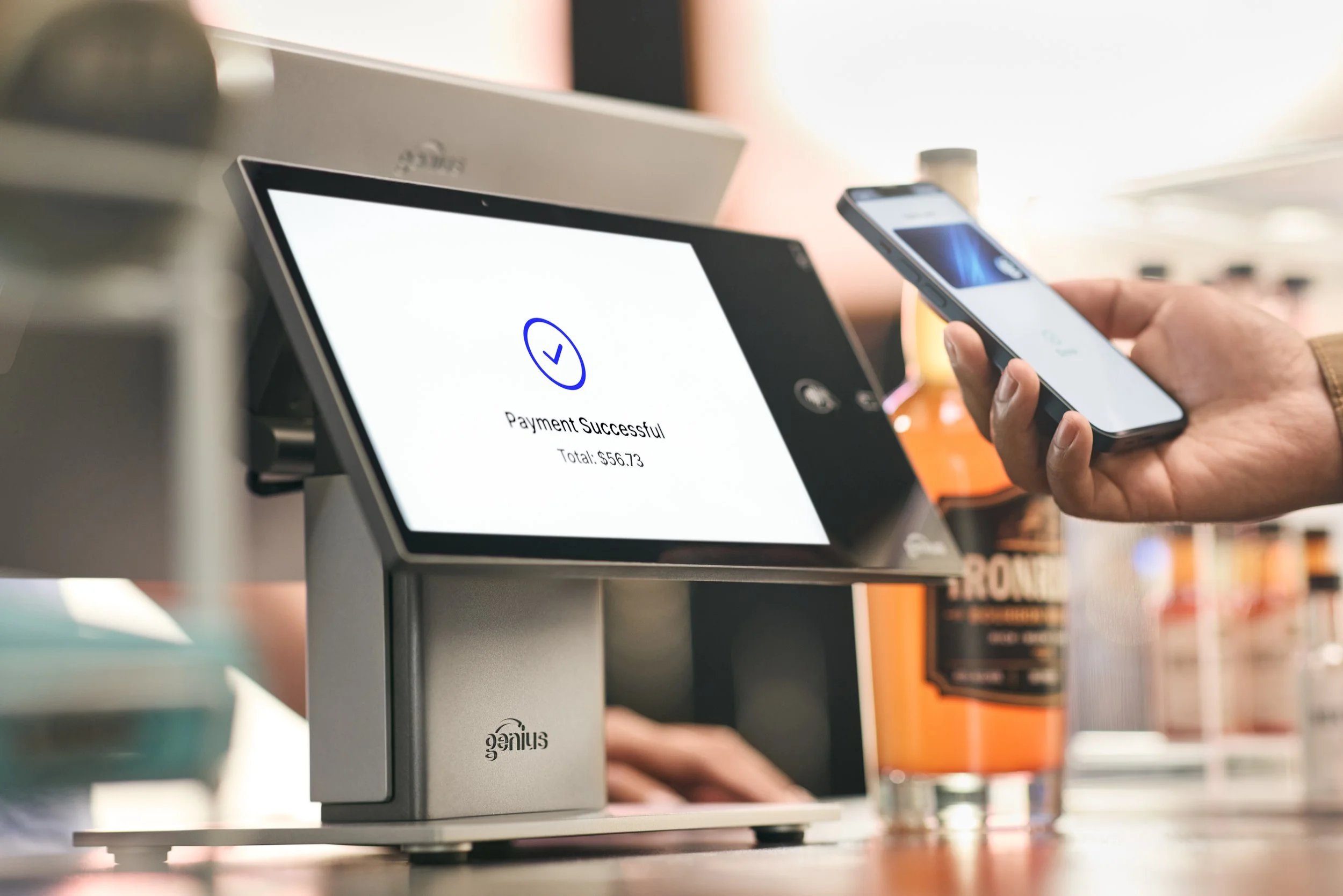 A payment terminal displaying a successful payment message and a total of $56.73, with a person holding a smartphone near the terminal.