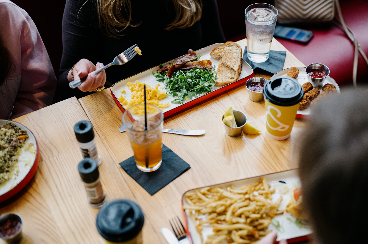 People having a meal at a restaurant table with various foods including scrambled eggs, toast, salad, fried chicken strips, and drinks.