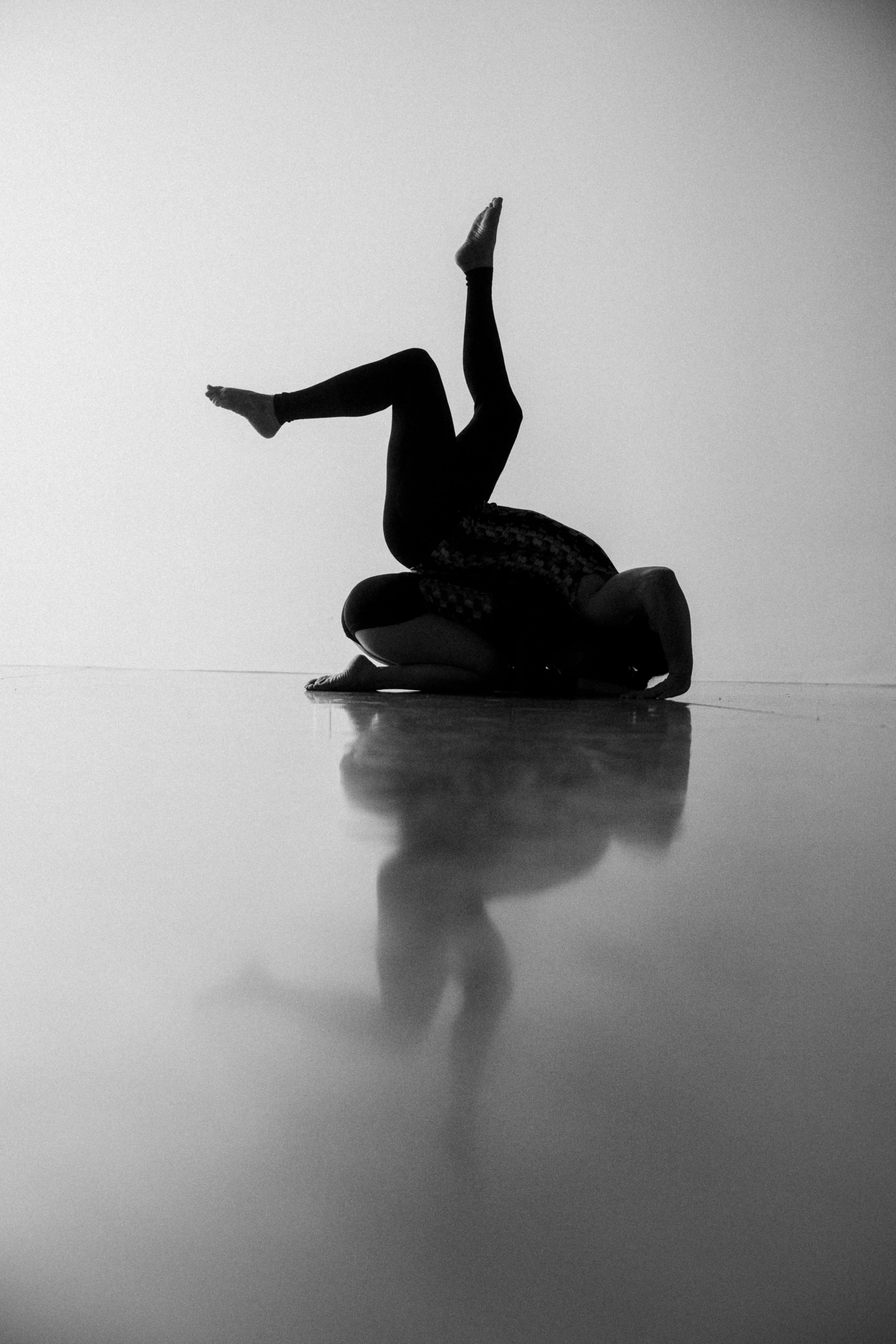 A person performing aerial yoga or acro yoga, lying on their stomach on another person's body, with their legs extended and raised in the air, in black and white with a high contrast effect.