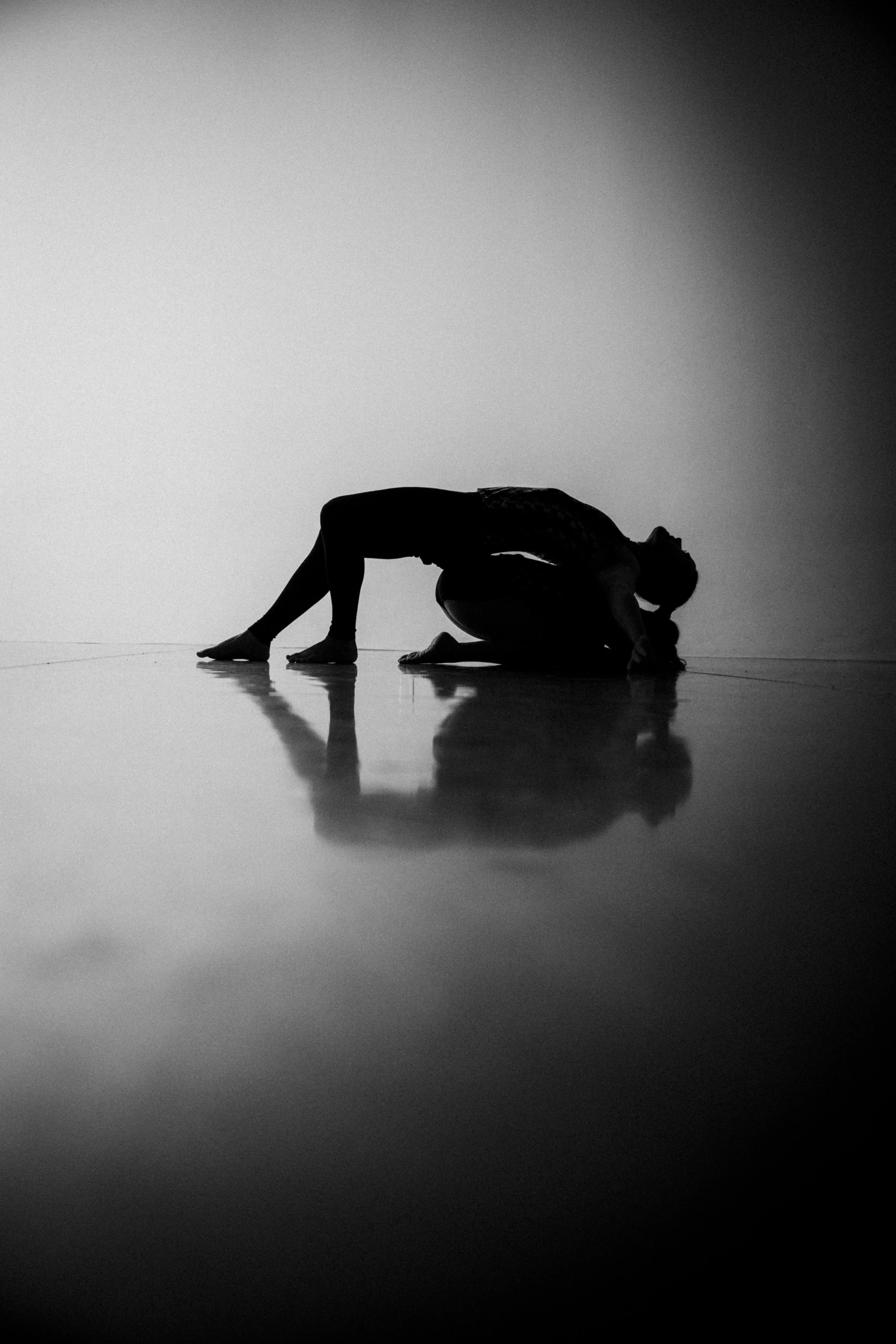 Silhouette of two people in a yoga pose on a reflective surface with a gradient background.