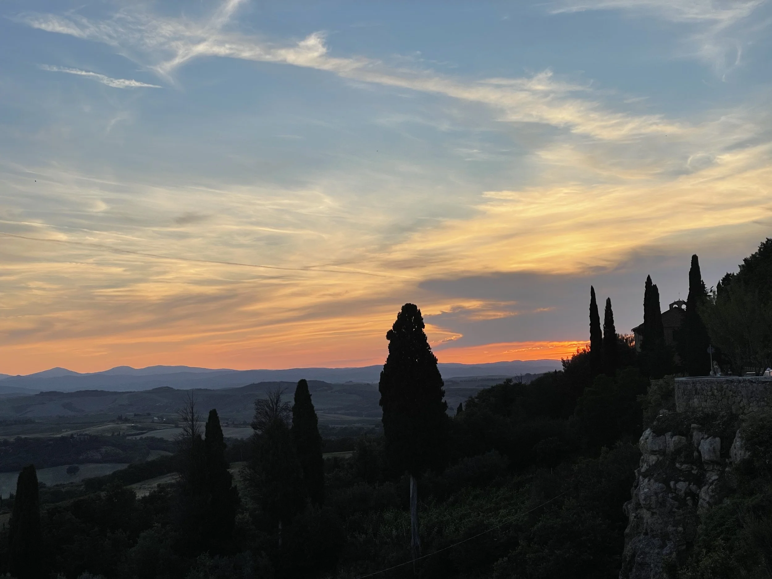Sunset over hilly landscape with trees in silhouette.