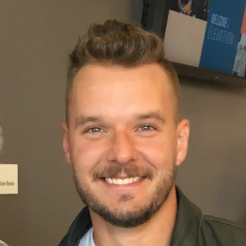 A smiling young man with short, styled brown hair and a beard.
